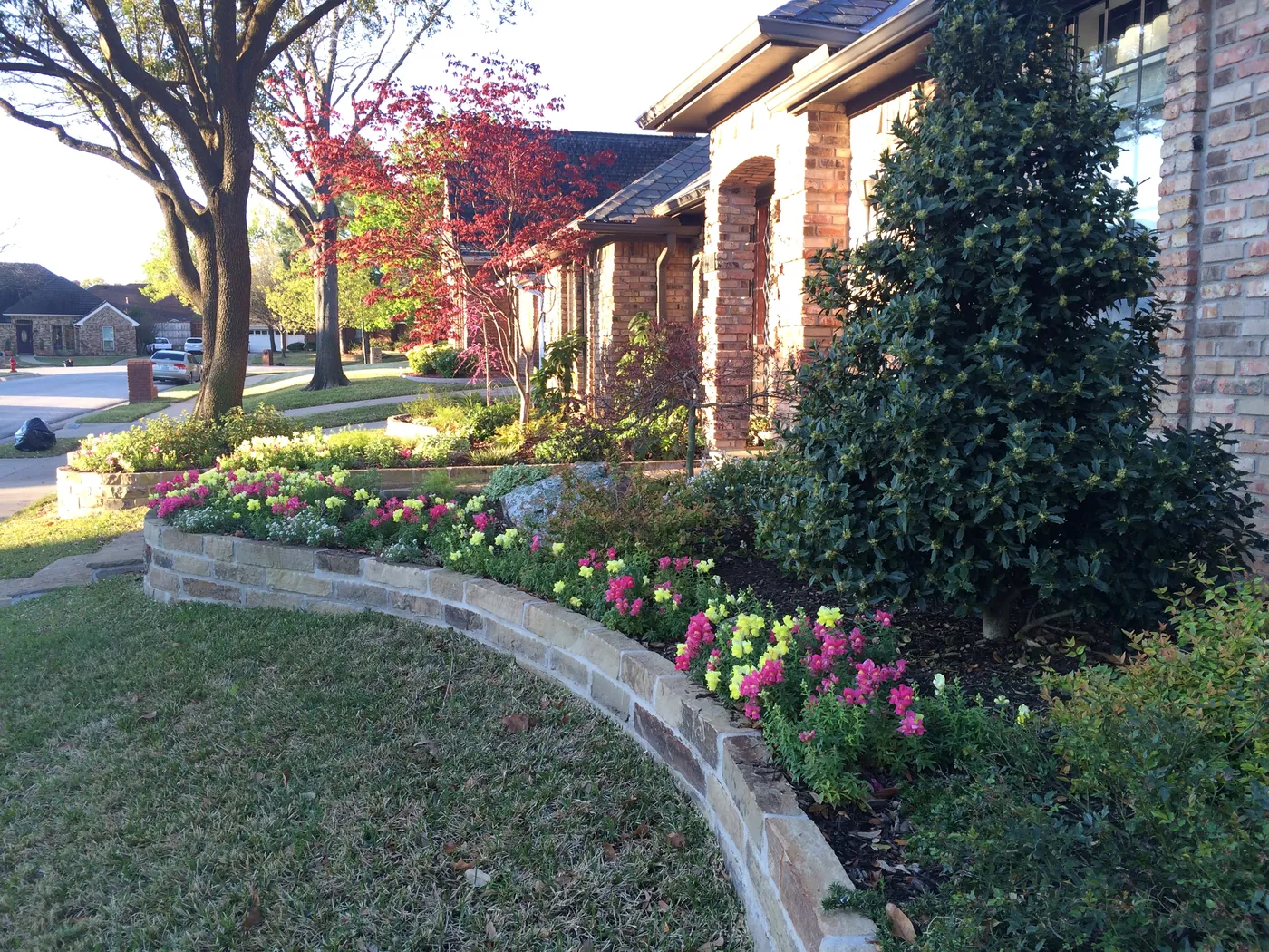 Curved stone planting beds filled with colorful seasonal flowers at a brick home