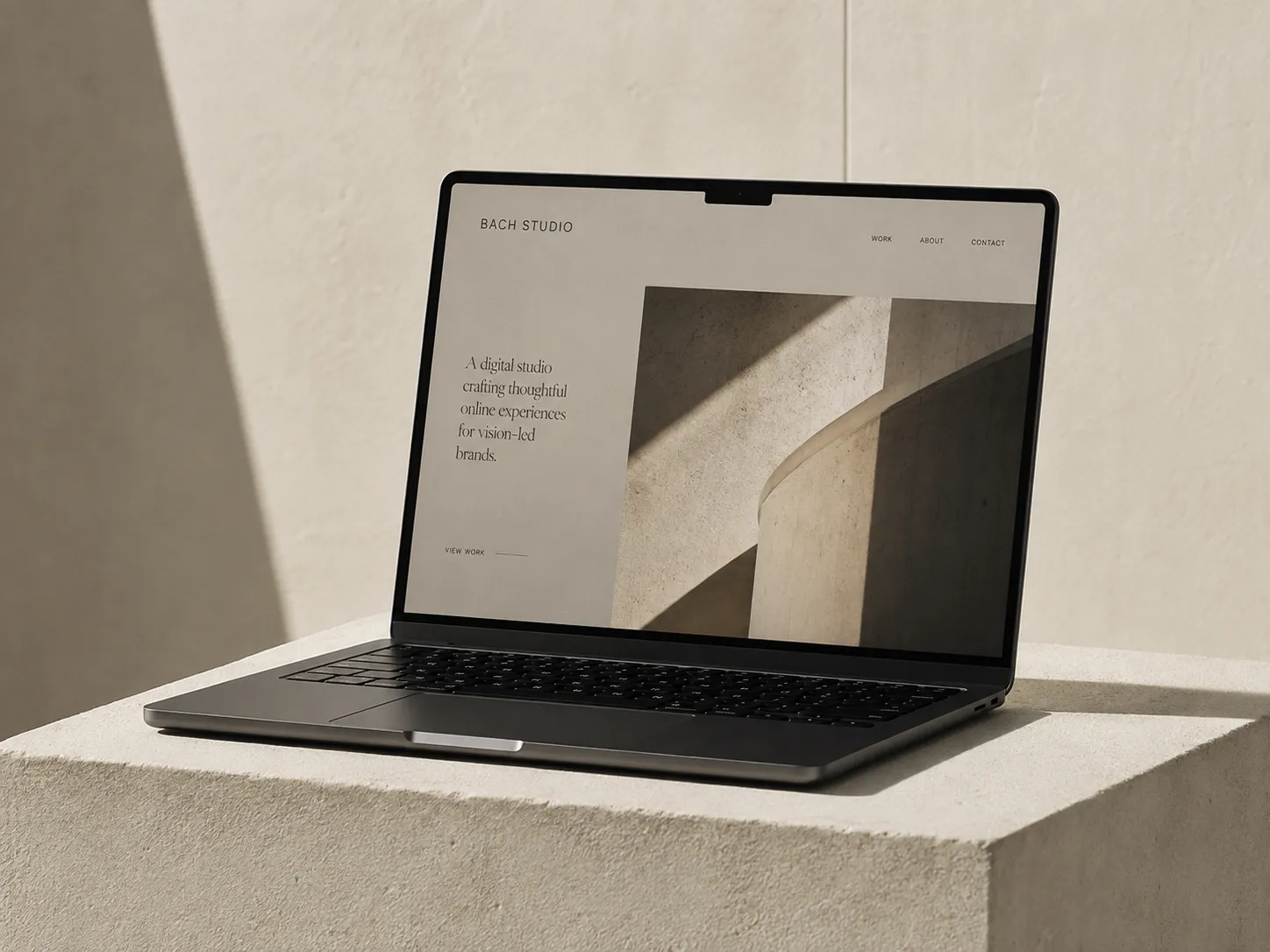 Laptop resting on a stone plinth in warm sunlight, displaying the BACH Studio website homepage.