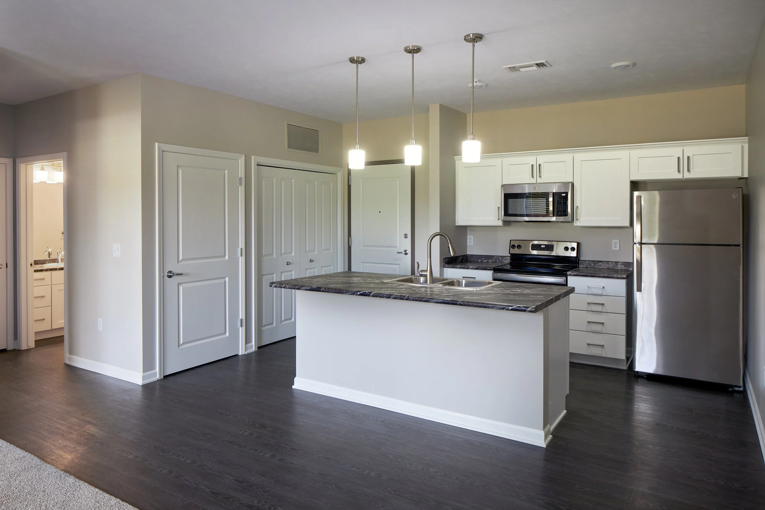 Deerfield Apartments kitchen in Fremont with white cabinets, a dark island, stainless appliances and pendant lights