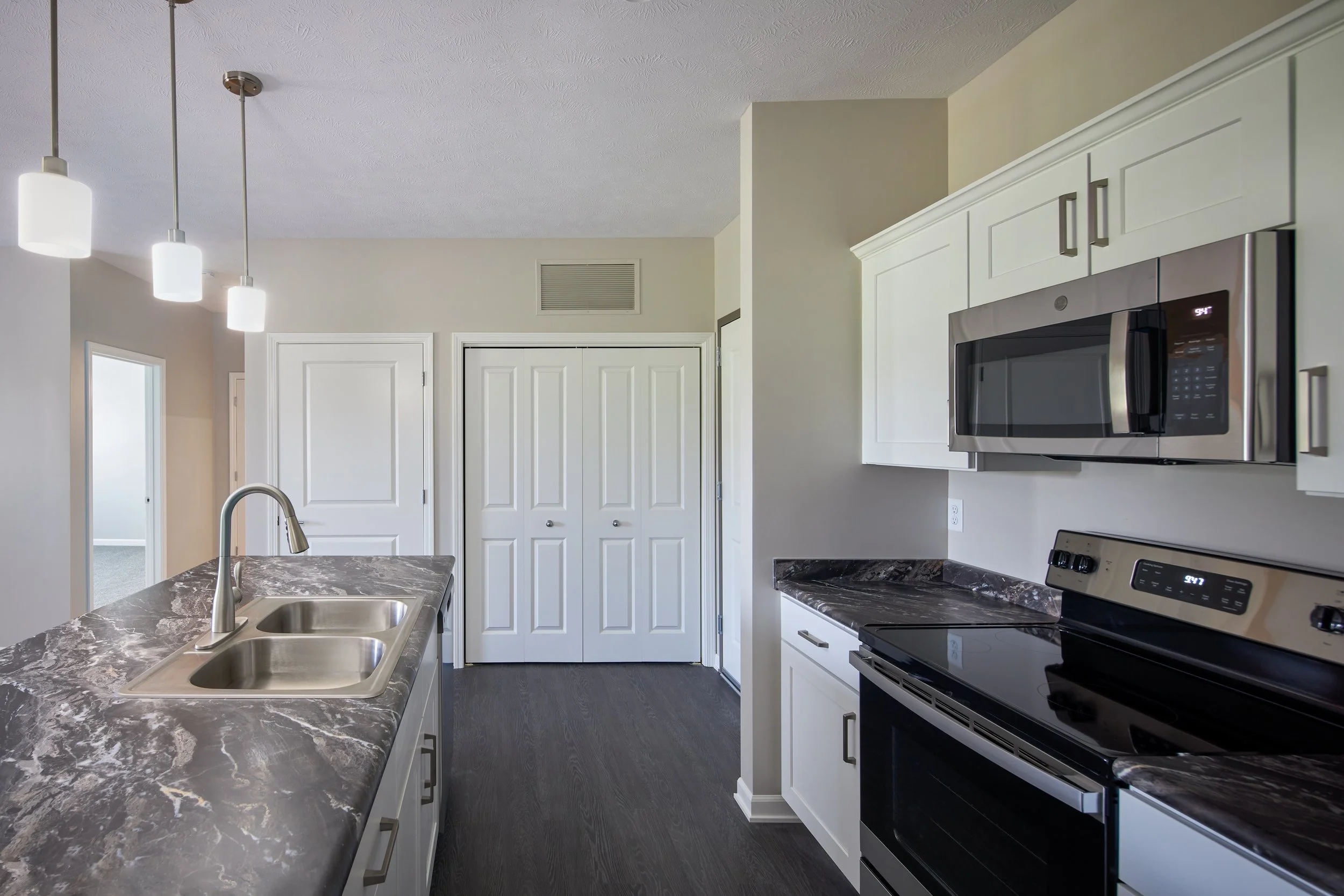 Apartment kitchen with white cabinets, stainless range and microwave, and pendant lighting over the sink