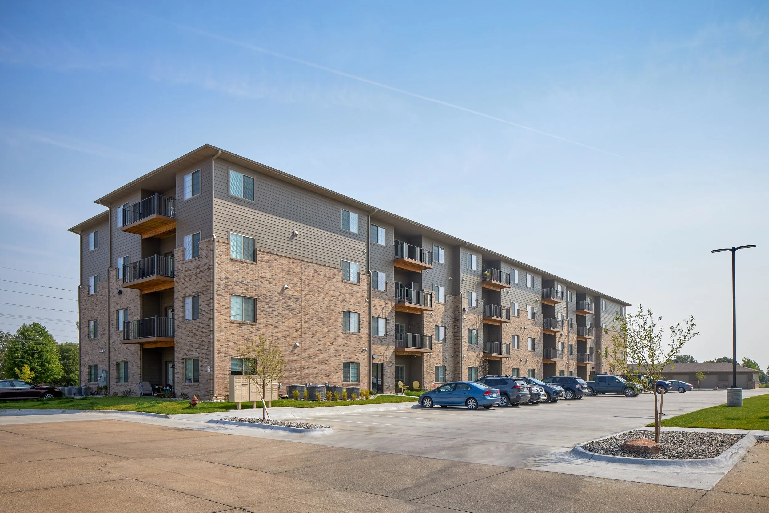 Exterior of the four-story Deerfield Apartments building with balconies and a parking lot