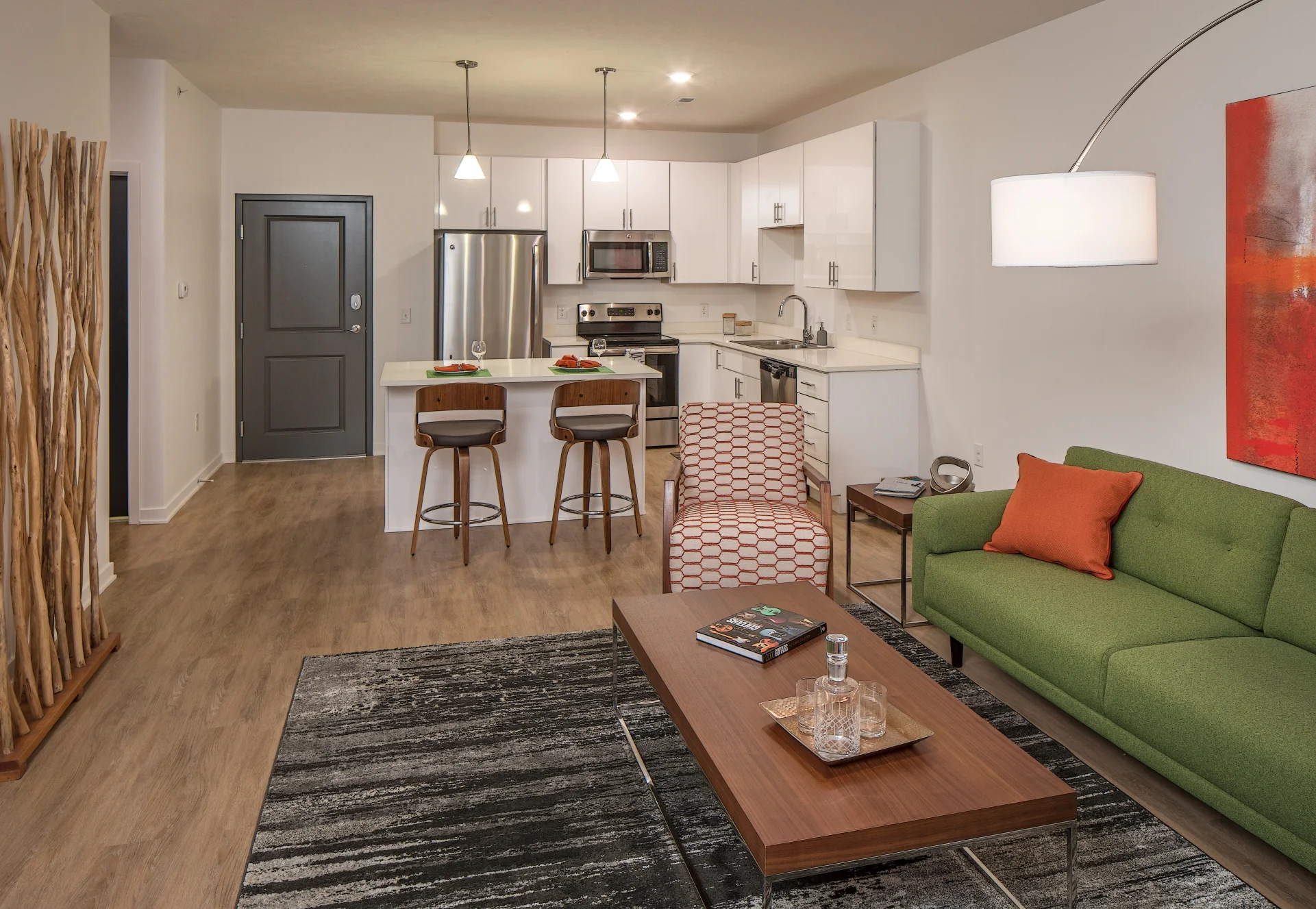 Model apartment living room with a green sofa, wood floors and an open kitchen with white cabinets