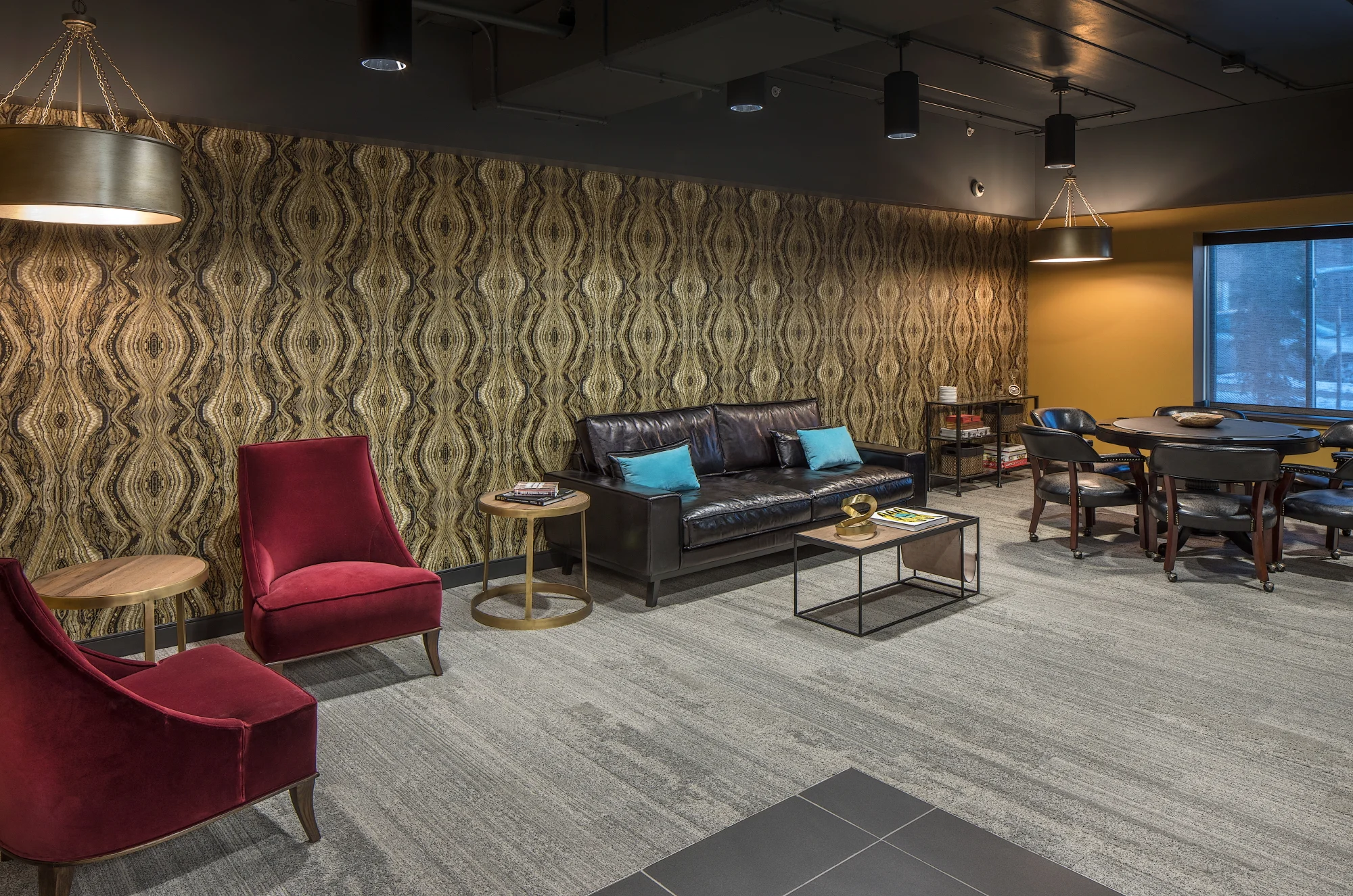 Game room with a poker table, leather sofa, red velvet chairs and patterned accent wallpaper
