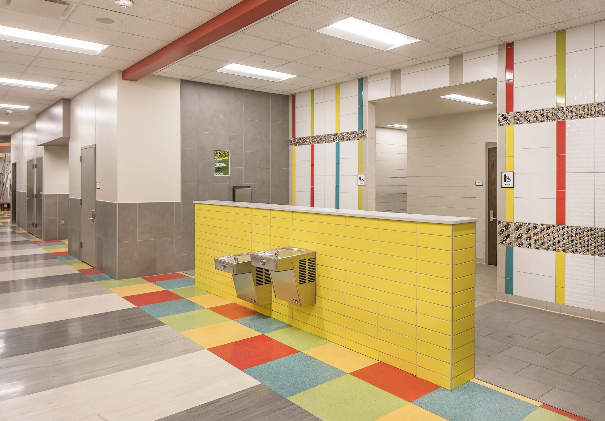 Hallway with a yellow tile drinking fountain wall and colored stripes