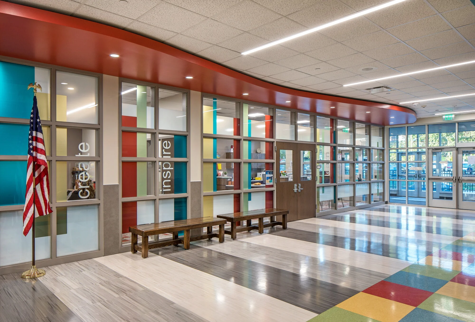 School entry lobby with a colorful checkered floor, orange accent wall and wood bench