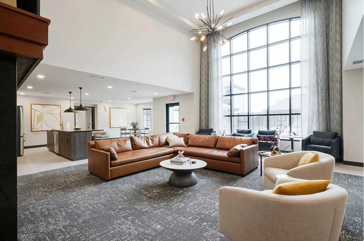 Two-story resident lounge with tall windows, cognac leather sofas and a modern chandelier