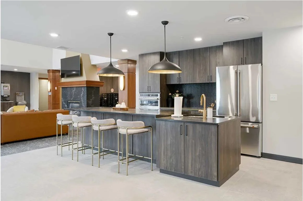 Community kitchen with a dark wood island, bar stools, pendant lights and stainless appliances