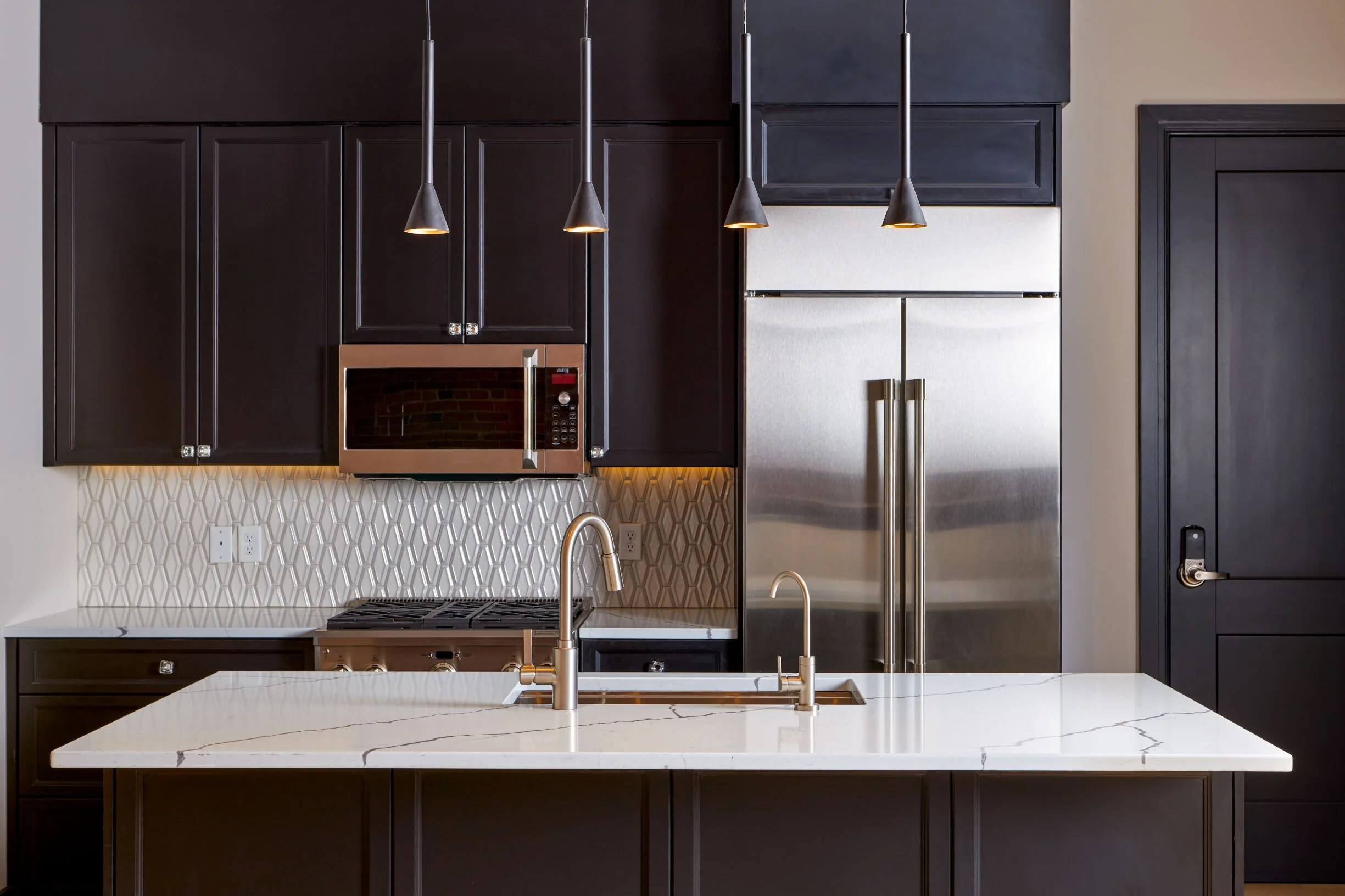 Loft kitchen with black cabinets, marble island, gold pendant lights and stainless appliances