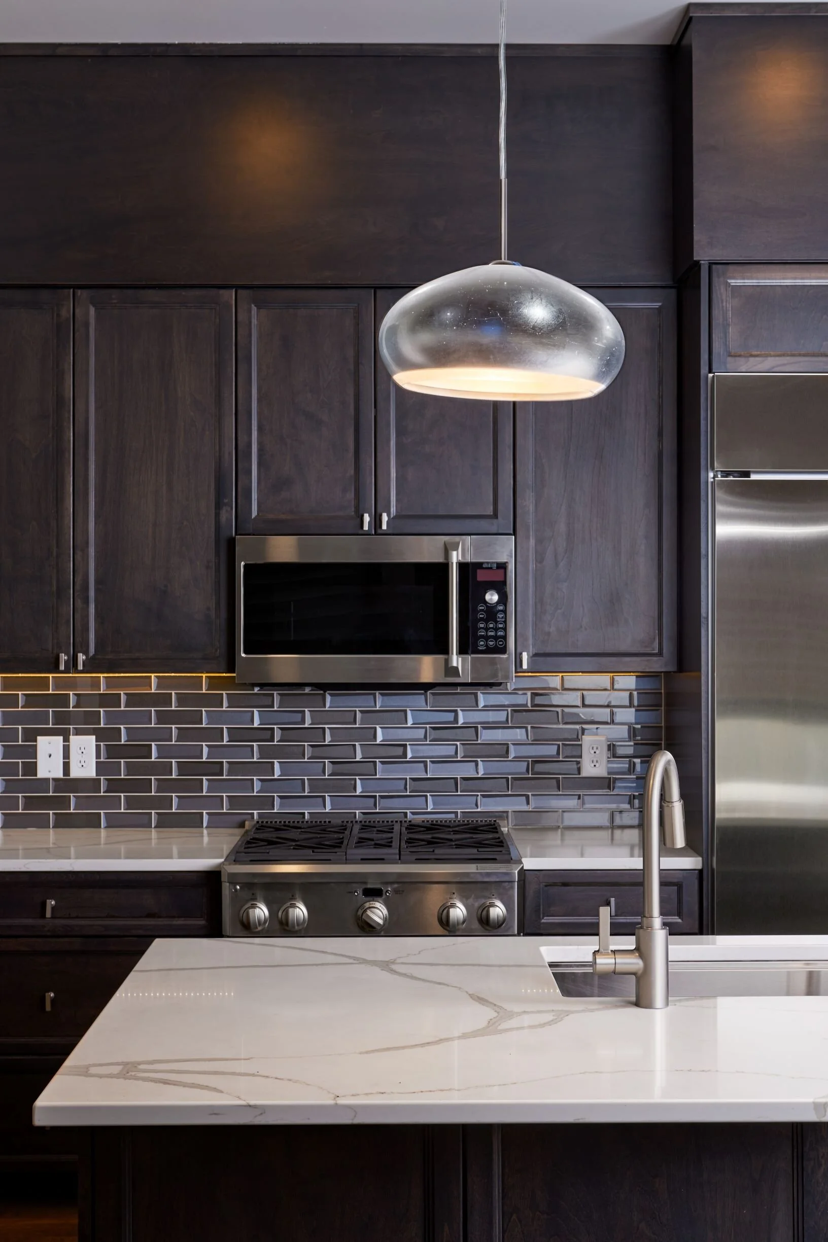 Kitchen detail with black cabinets, blue subway tile backsplash and marble countertop