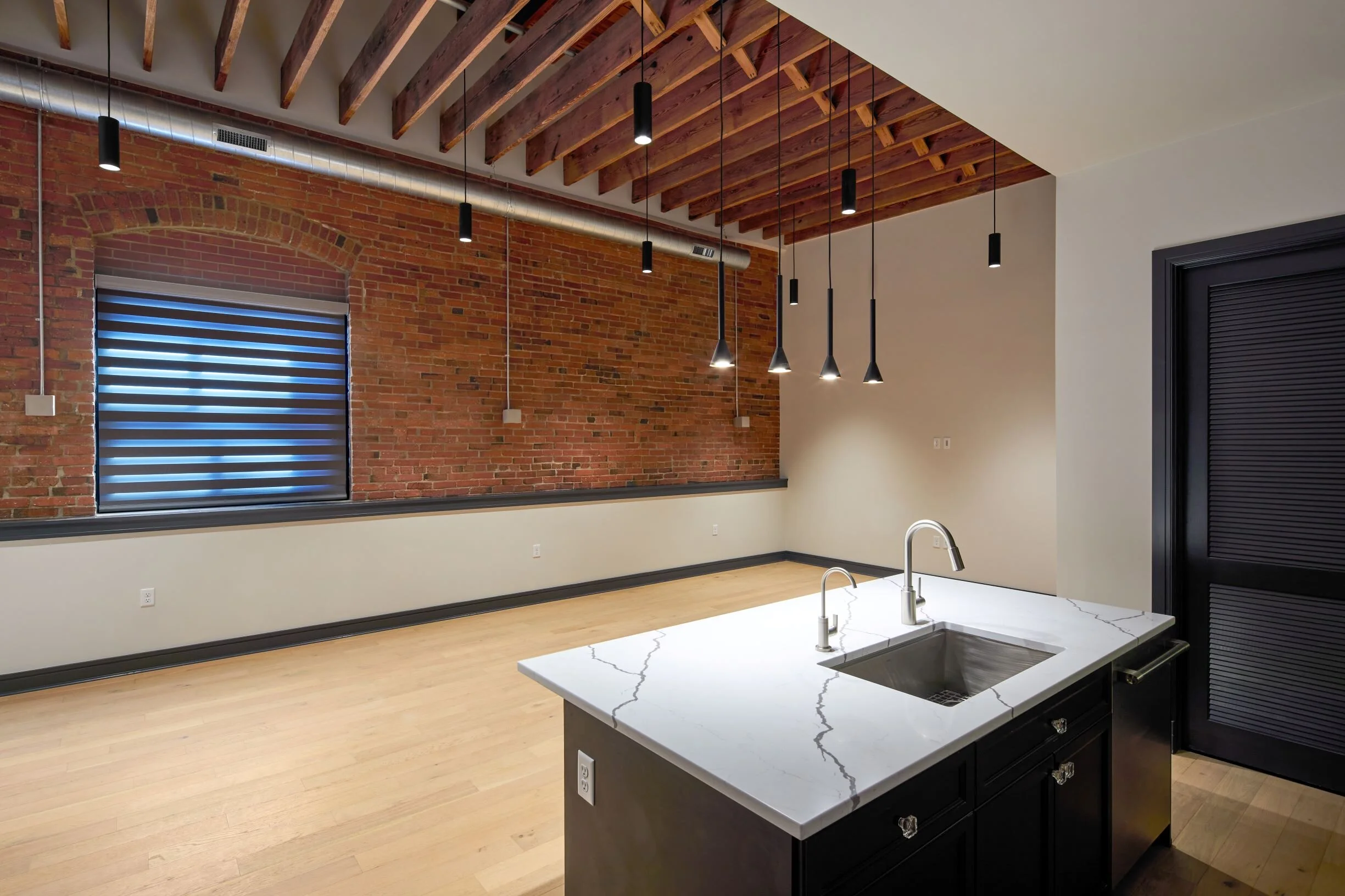Open loft living space with exposed brick, timber ceiling beams and a kitchen island