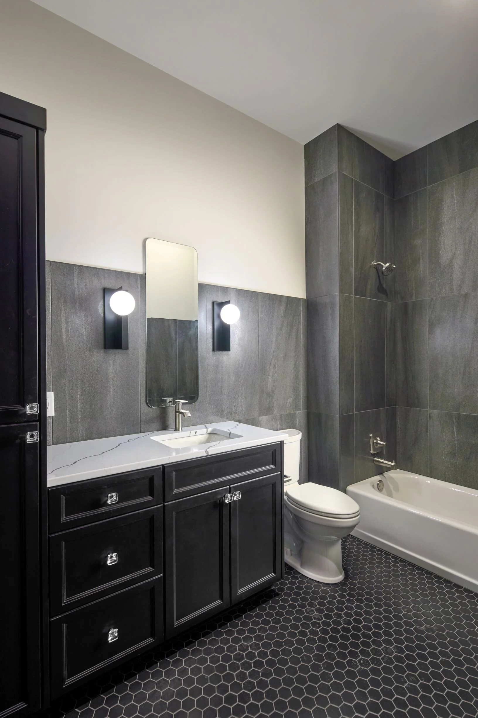 Loft bathroom with dark vanity, tiled tub surround and patterned floor tile