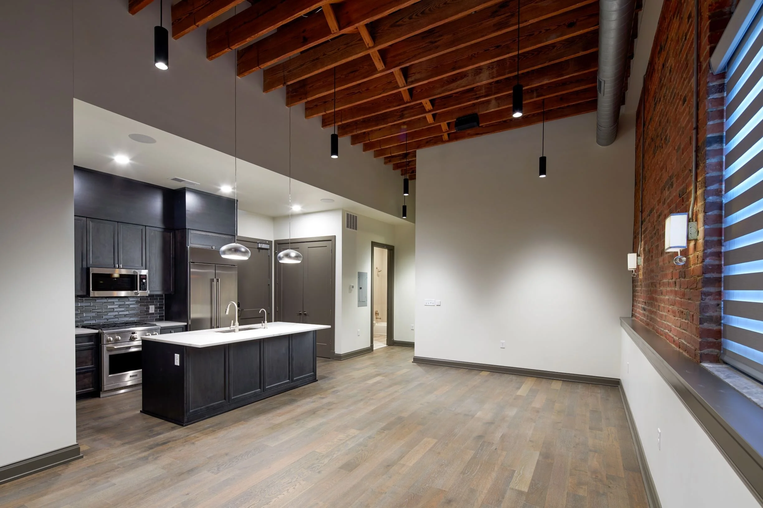 Loft kitchen and living area with exposed brick, wood floors and black cabinetry