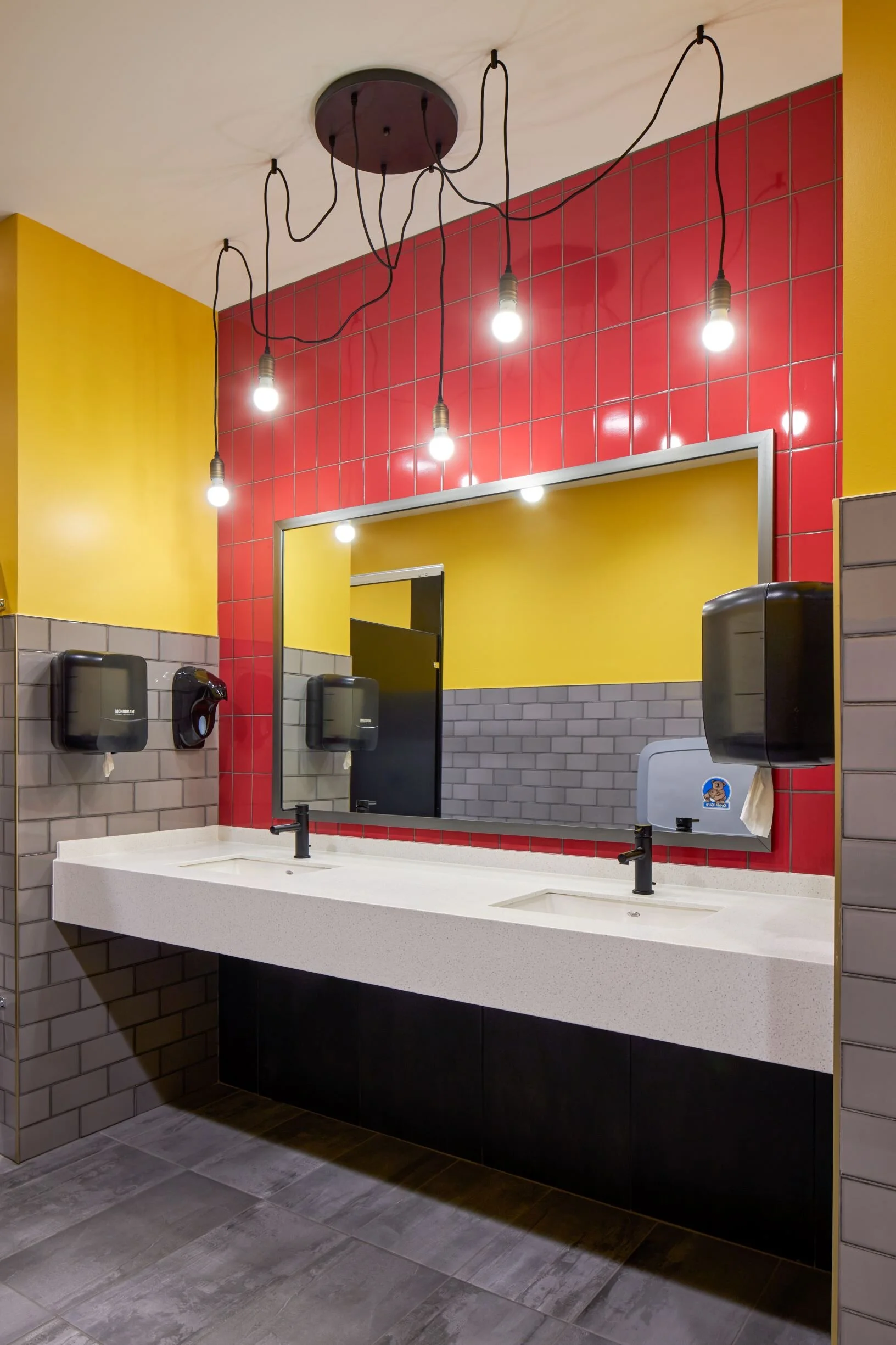 Restroom with a yellow accent wall, red tile and Edison bulb mirror lights