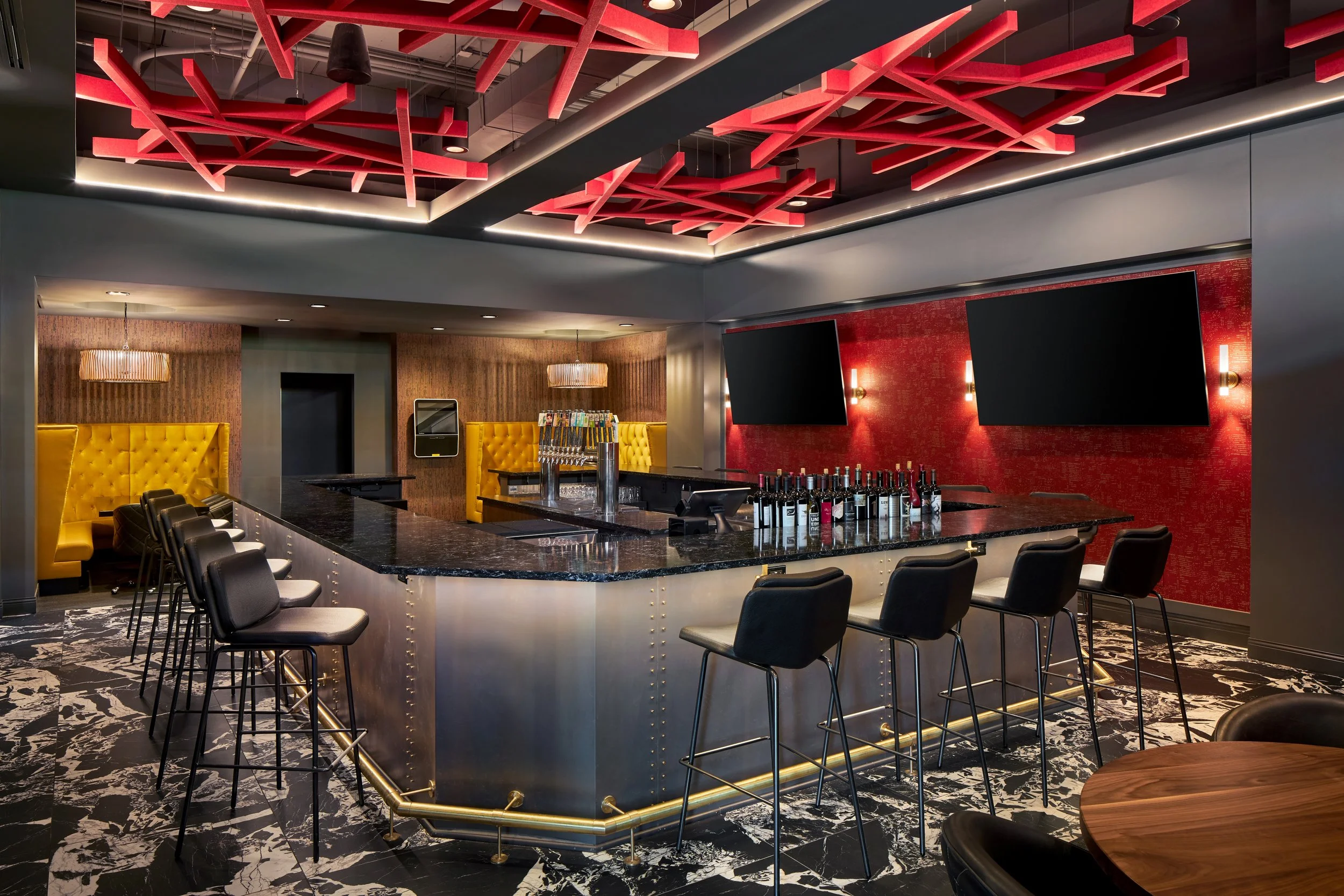 Bar with a red sculptural ceiling, black stools and a lit bar top
