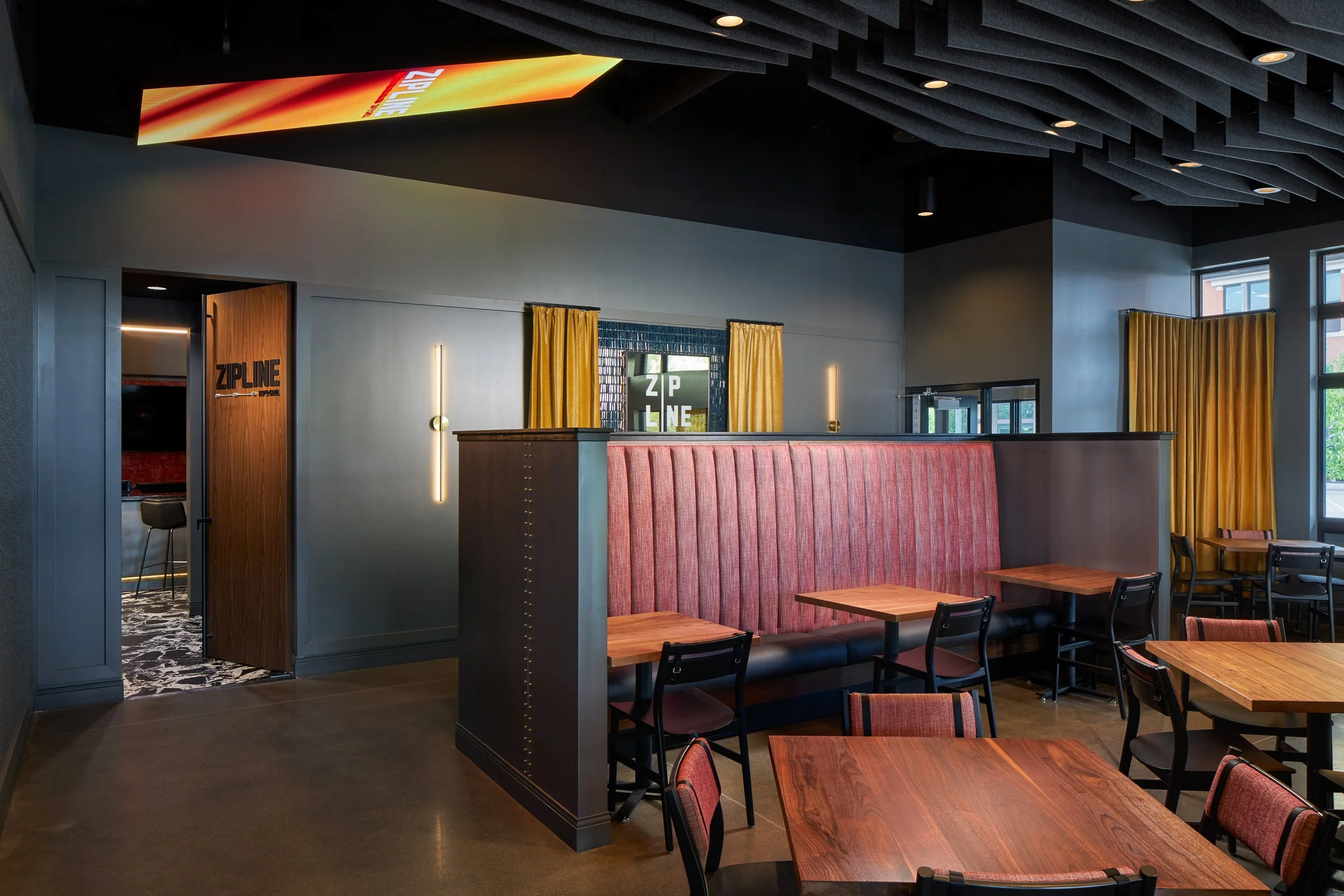 Dining area with wood tables, red slat wall and gold drapery