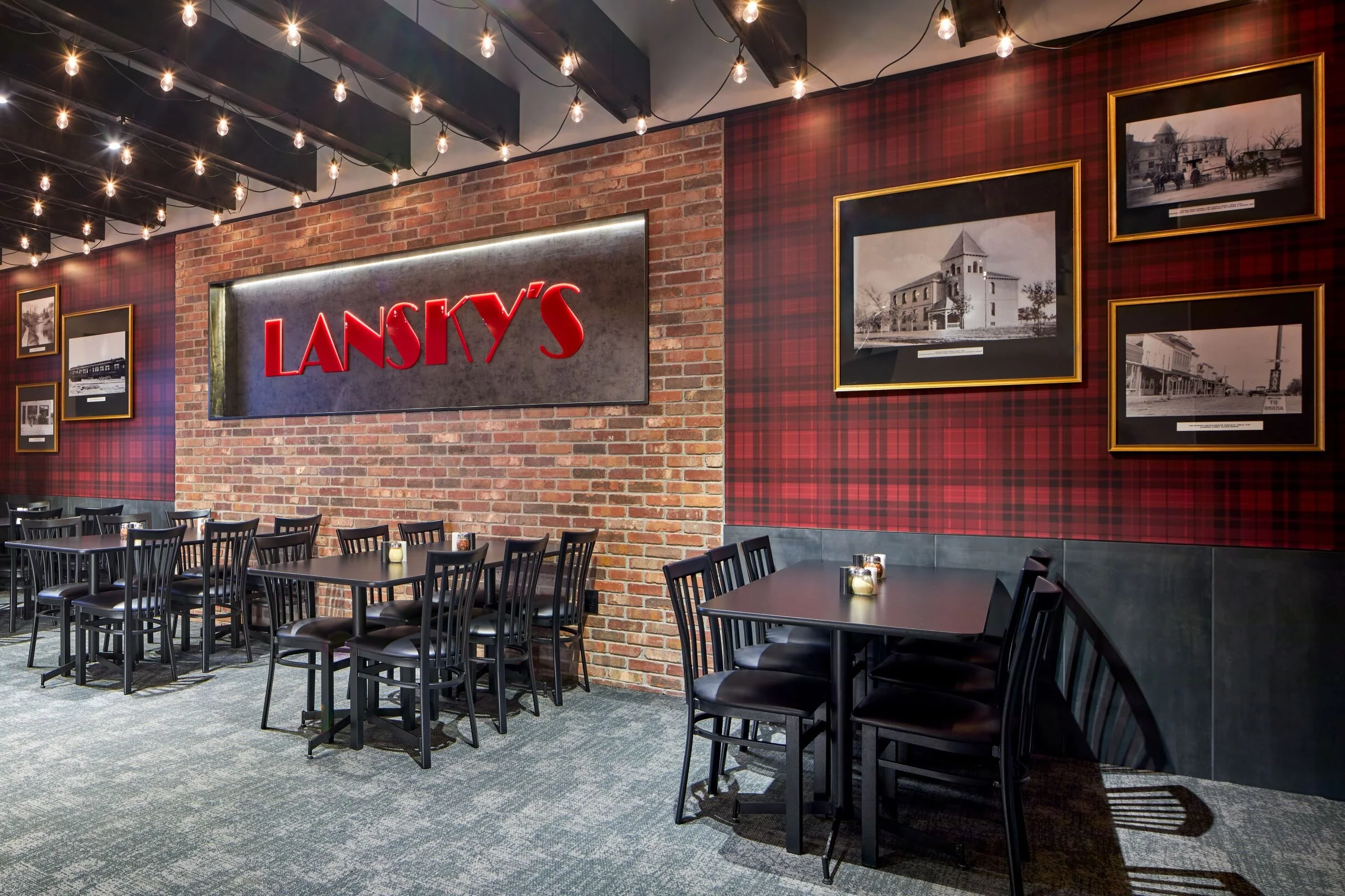 Dining room at Lansky's in Gretna with a red brick wall, plaid wallpaper and framed historic photos