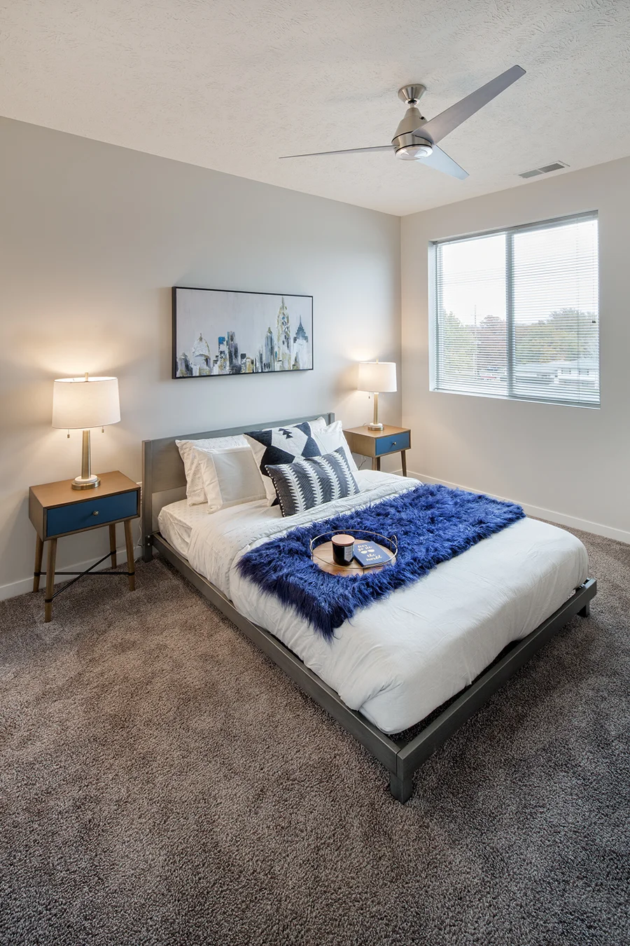 Apartment bedroom with a white bed, navy throw and a window with city views