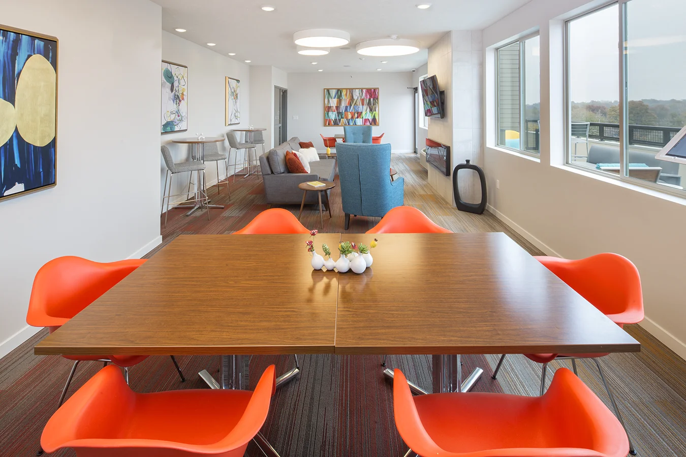 Community dining table with orange chairs overlooking lounge seating and city views
