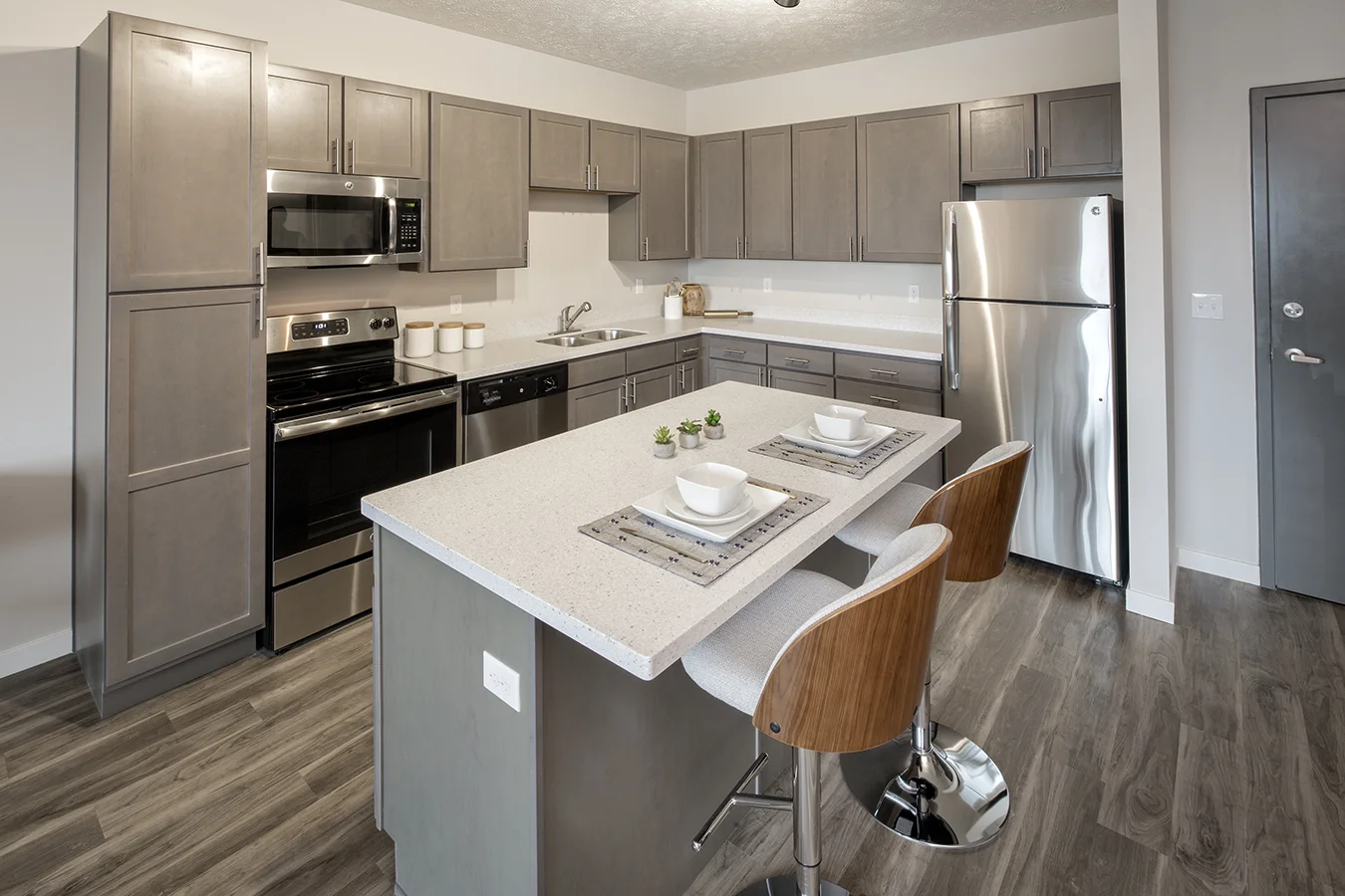 Apartment kitchen with gray cabinets, white island with bar stools and stainless appliances