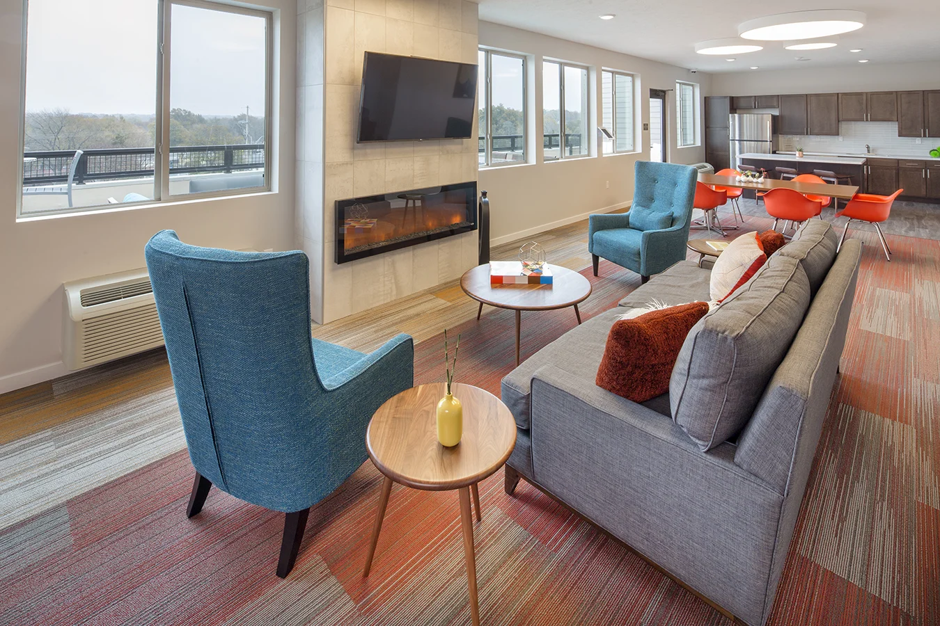 Clubroom lounge with teal wingback chairs, gray sofa and a linear fireplace under a wall-mounted TV