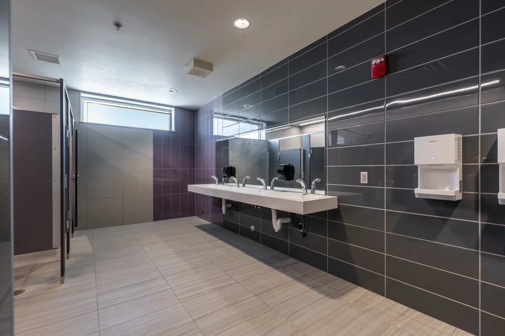 School restroom with dark gray tile, floating sinks and wood-look floor