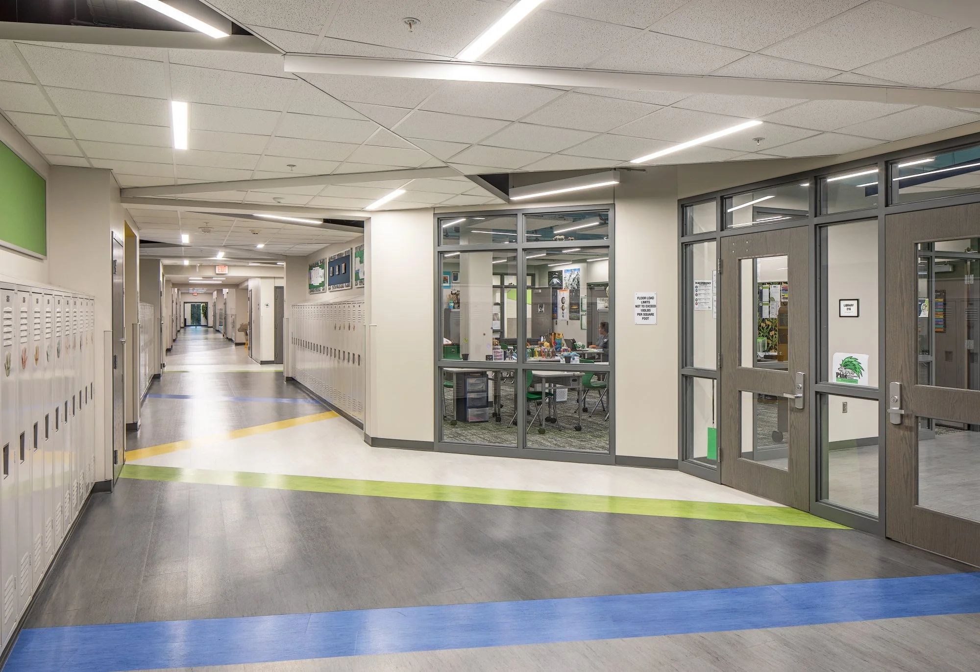 Hallway with lockers, green and blue floor stripes and glass-walled rooms
