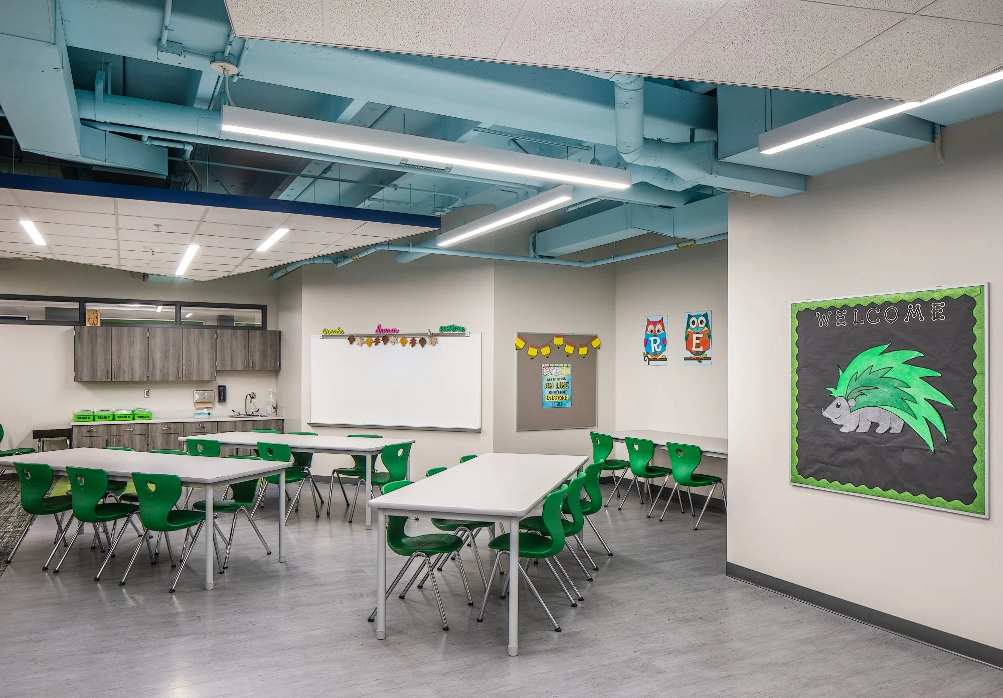 Classroom with green student chairs, white tables and blue ceiling beams