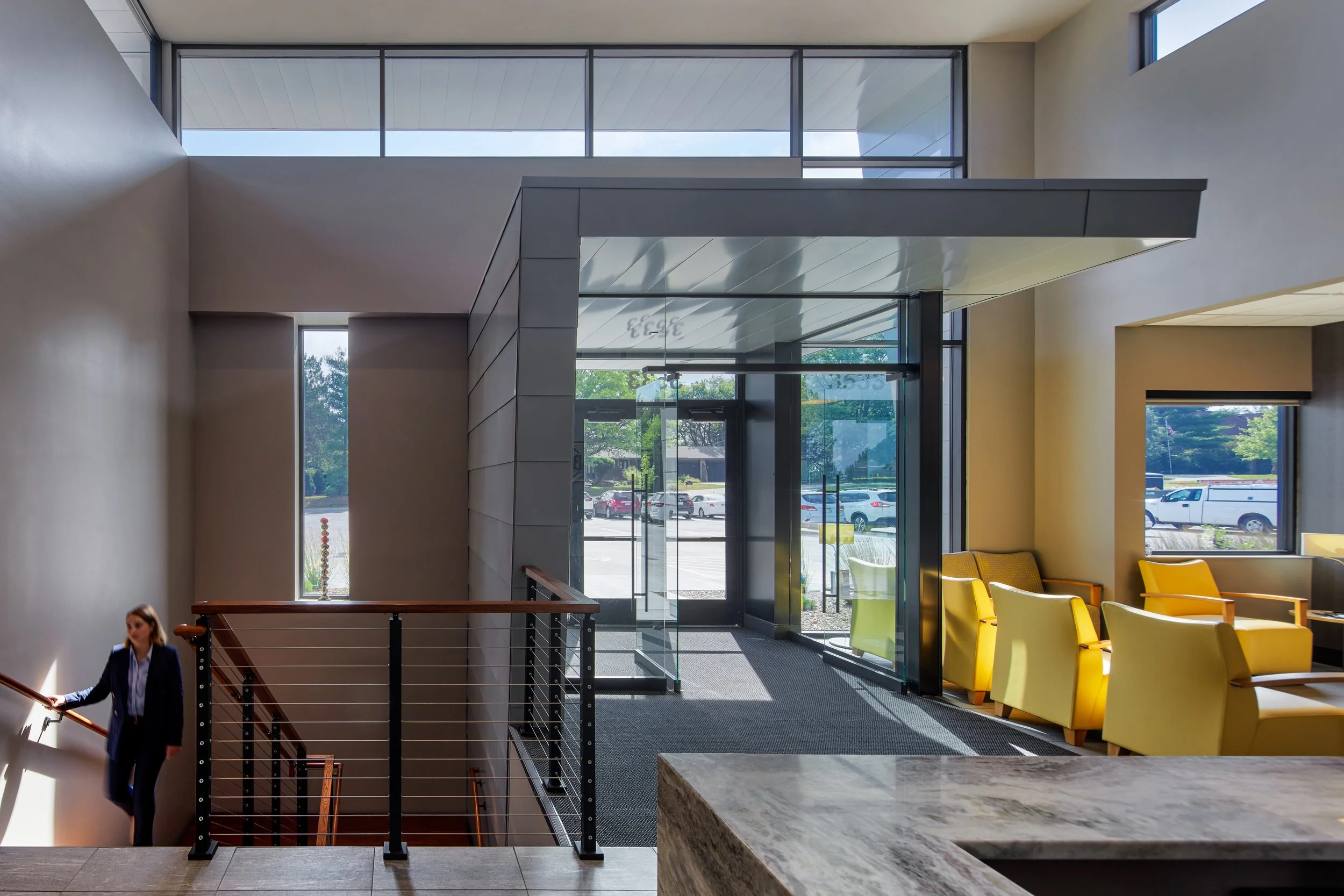 Two-story lobby at BMG CPAs in Lincoln with a stair, cable railing and yellow lounge chairs