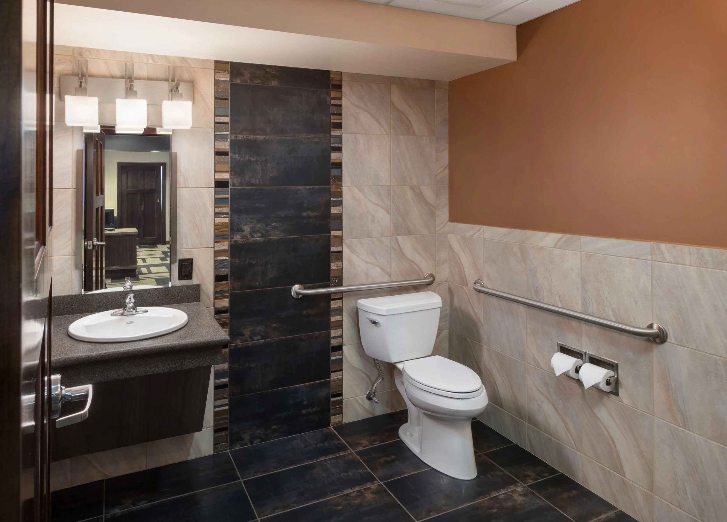 Accessible restroom with a wood vanity, tile wall and grab bars