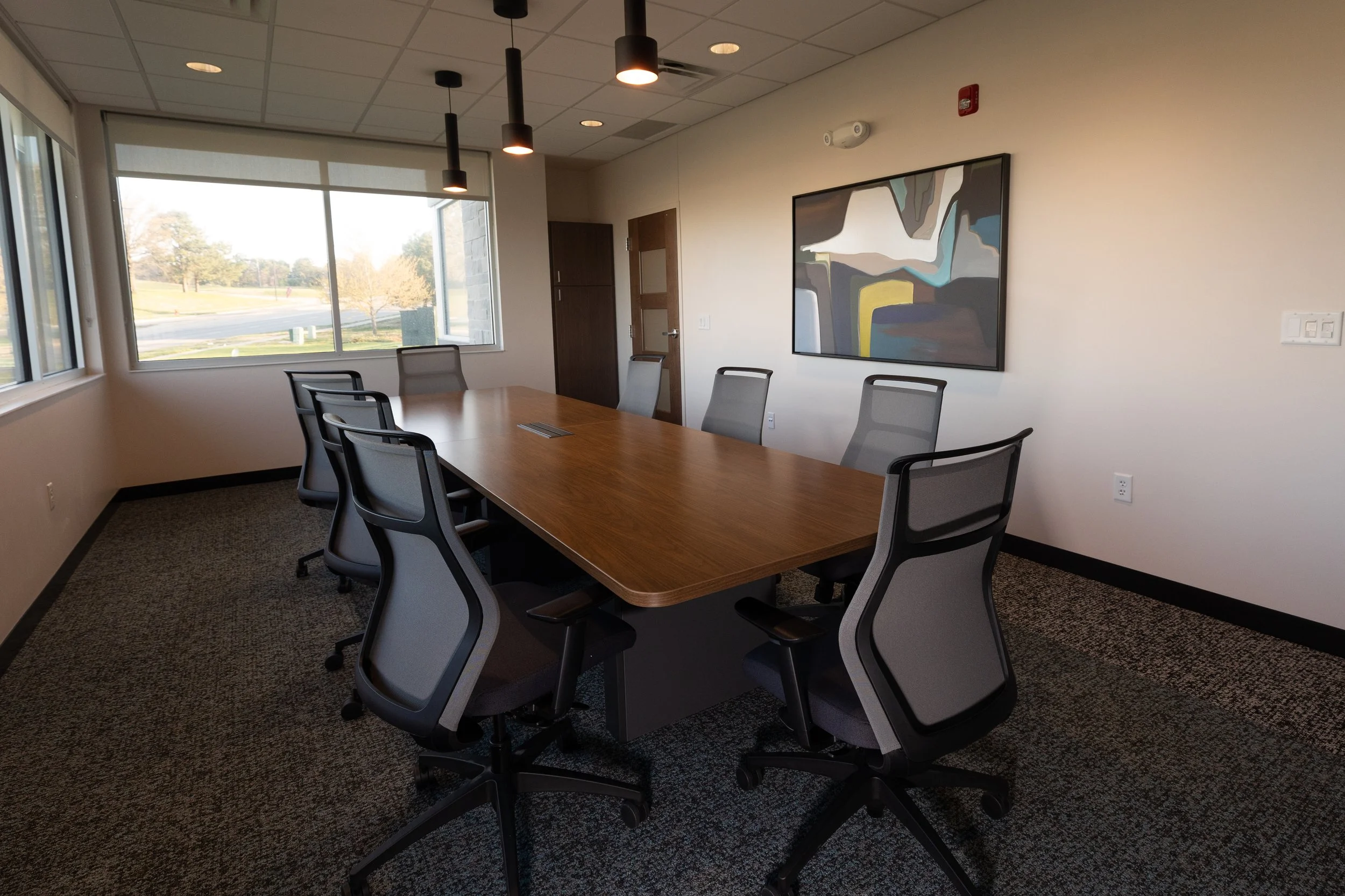 Conference room with a long wood table, mesh chairs and a window view