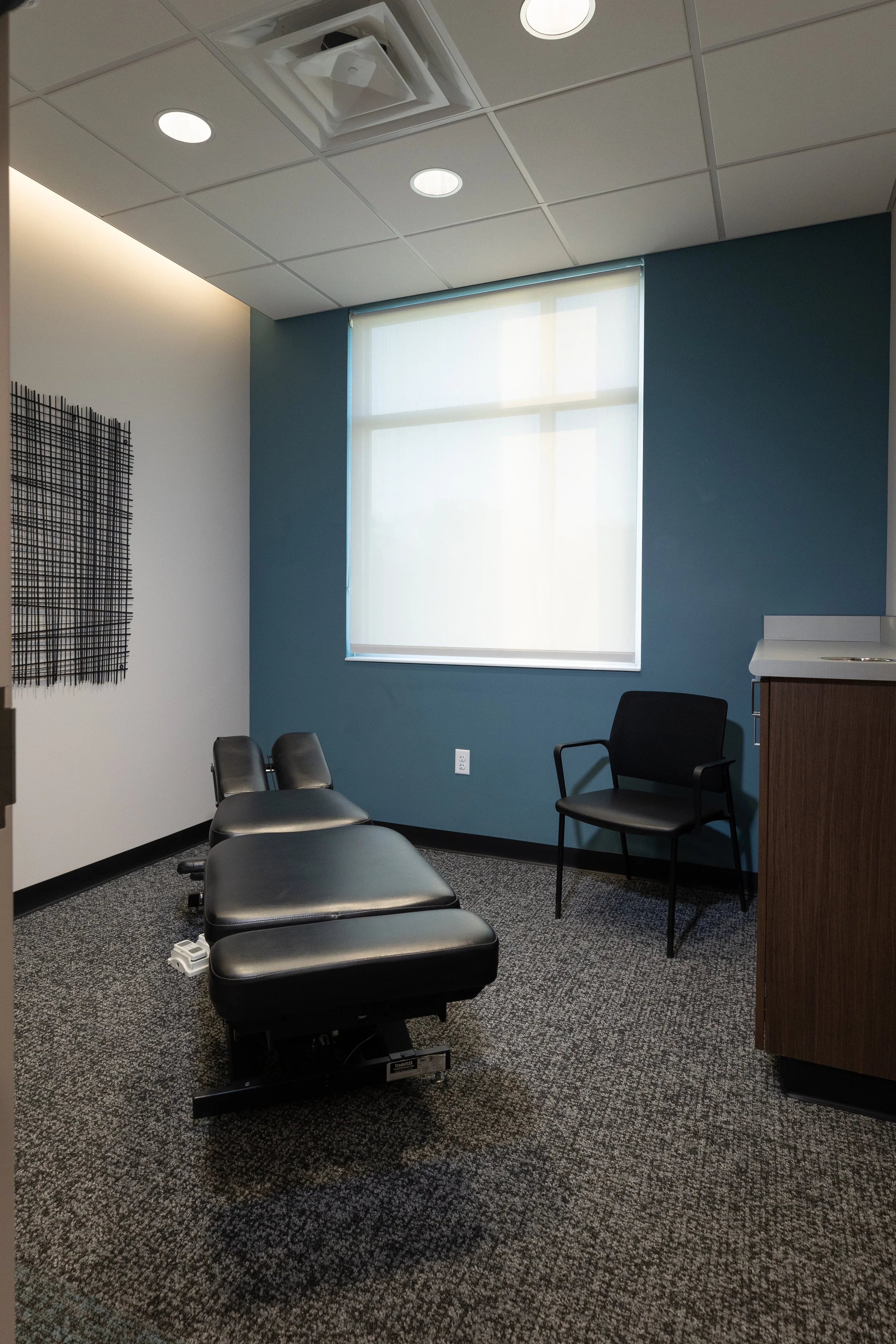 Treatment room with a chiropractic table and a dark teal accent wall