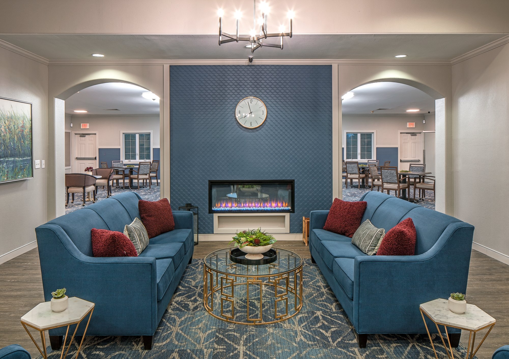 Kings Gate senior apartments lounge in Omaha with blue sofas facing a fireplace and a chandelier