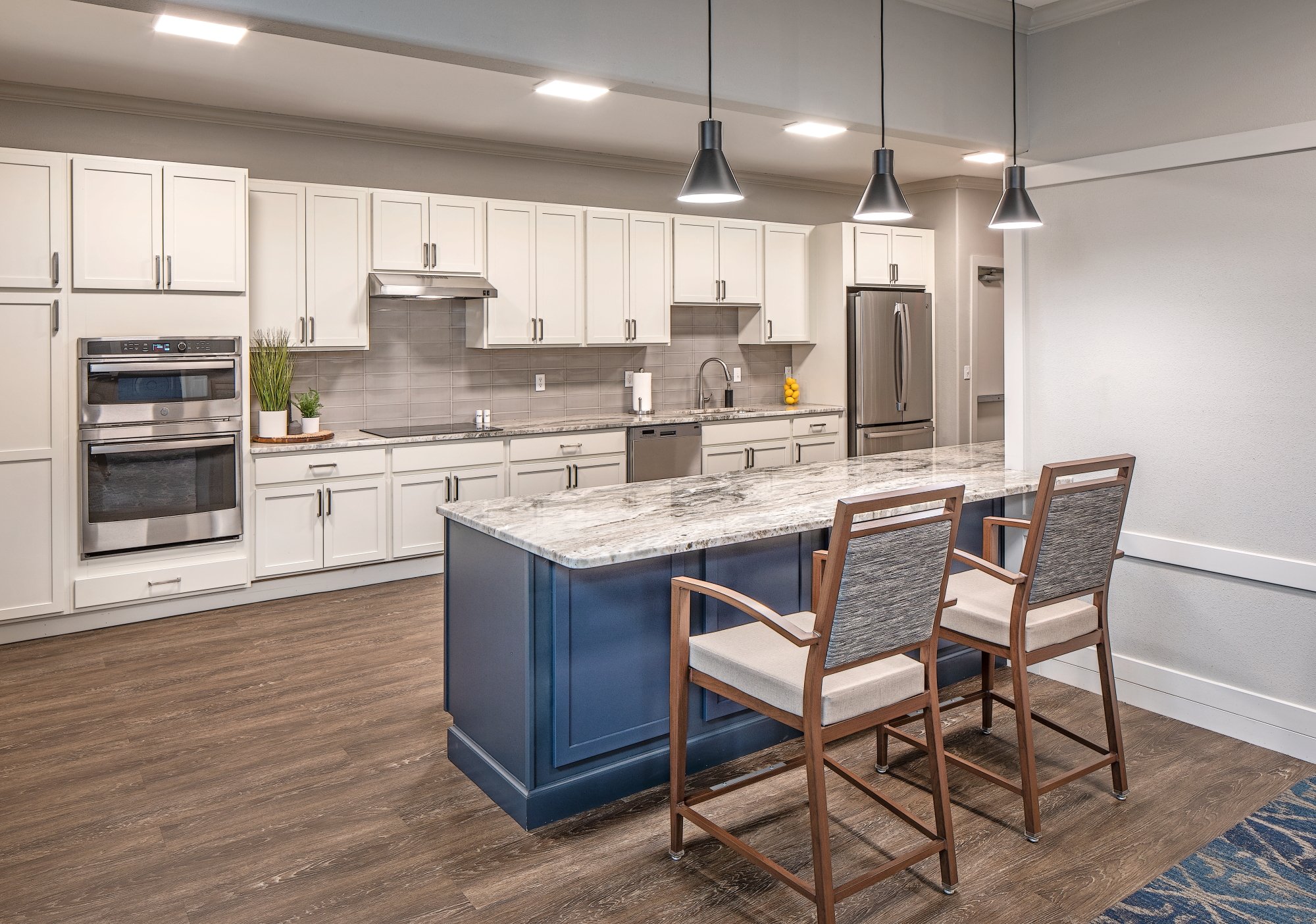 Community kitchen with white cabinets, a navy island and upholstered bar stools
