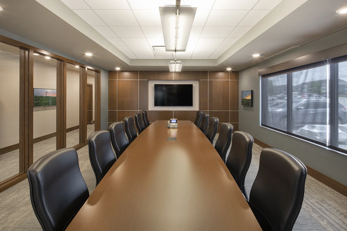 Boardroom with a long wood table, black leather chairs and wood paneled walls