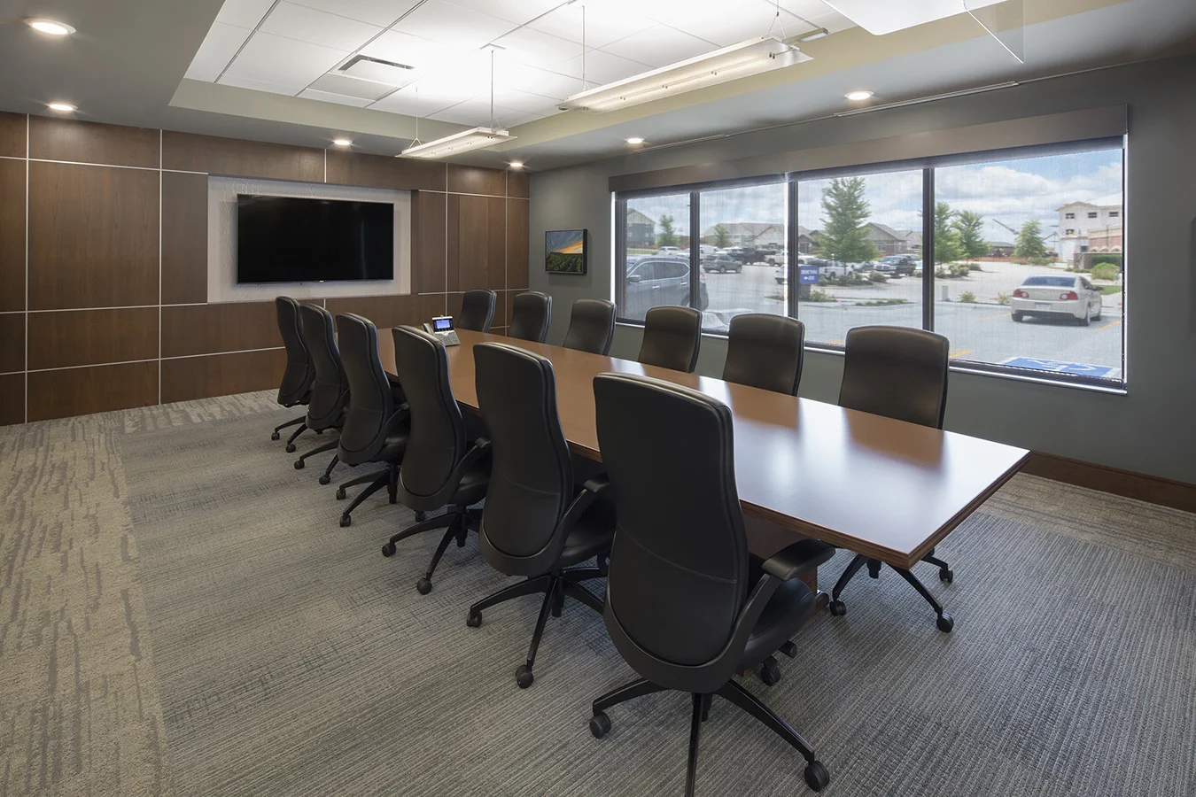 Conference room with a wood table, black chairs and windows overlooking the parking lot