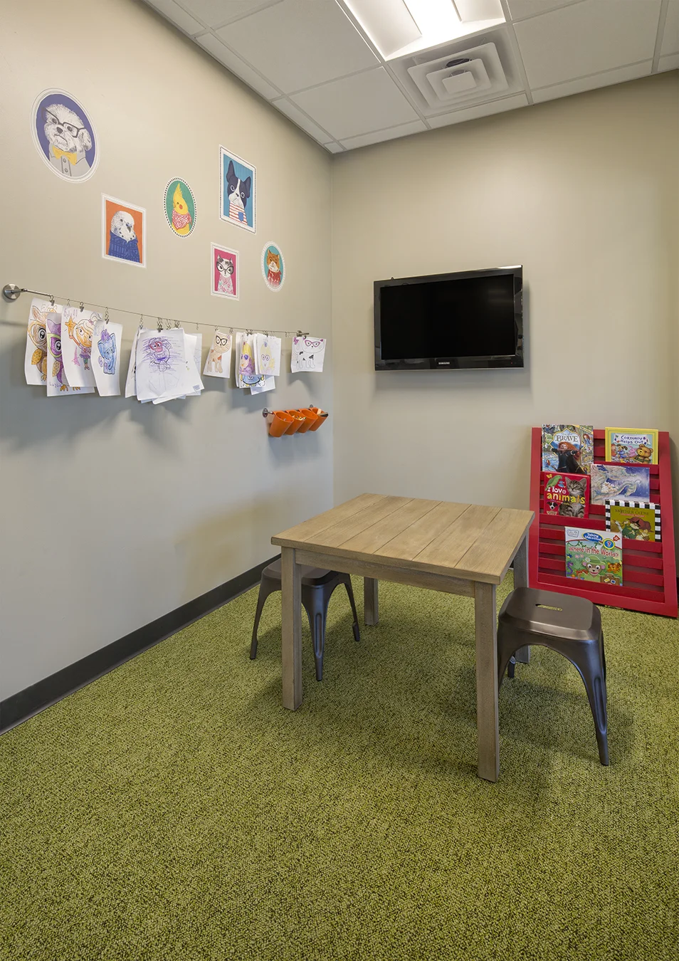 Children's play area with a small table, wall-mounted TV and green carpet