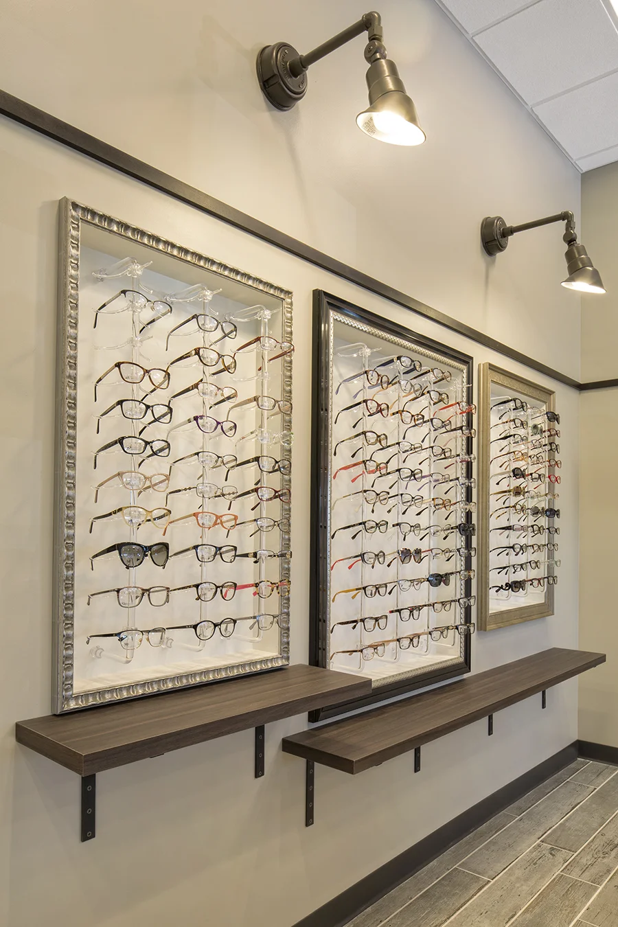 Eyeglass display wall with frames on lit panels and a wood ledge