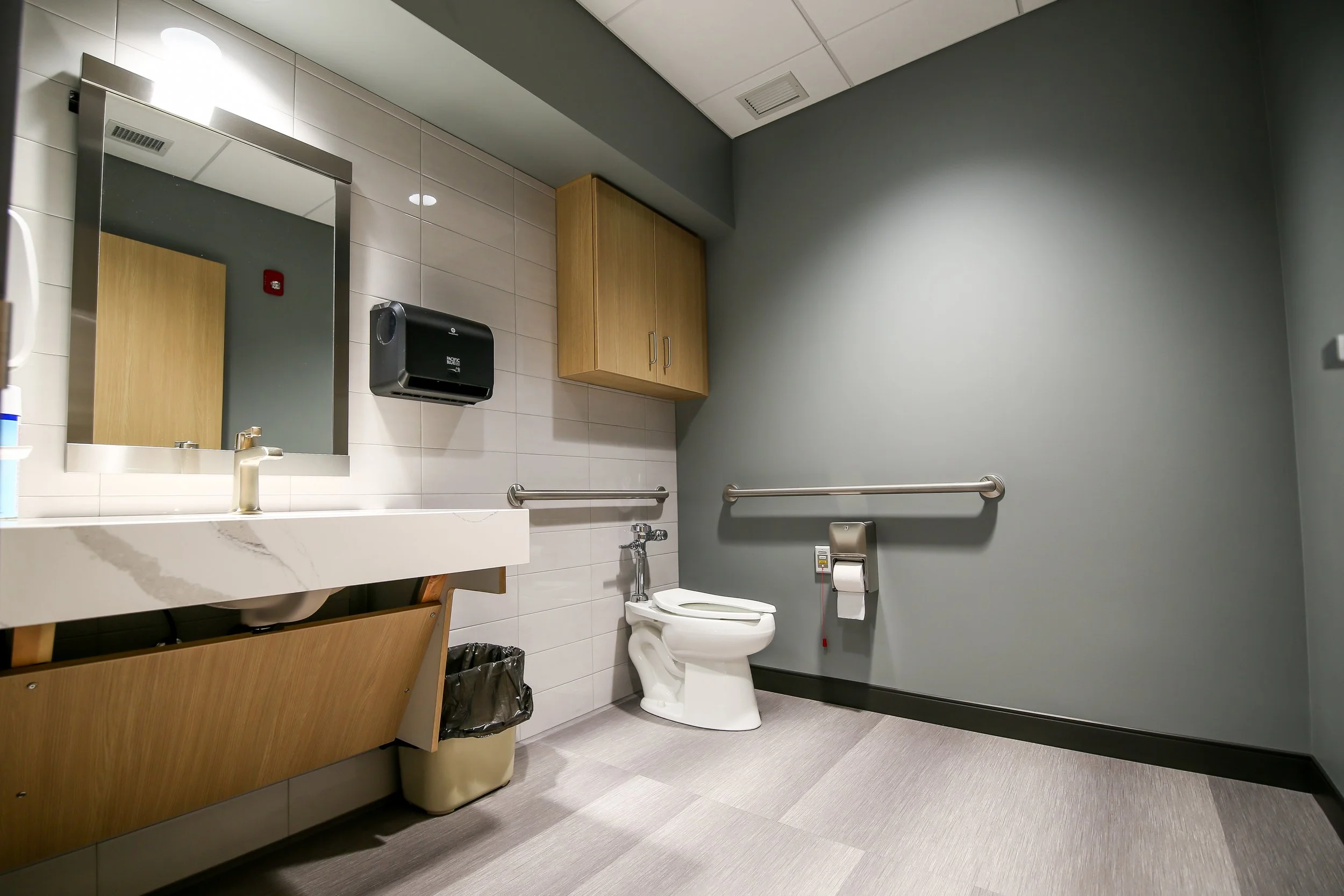 Accessible restroom with wood vanity, gray walls and grab bars