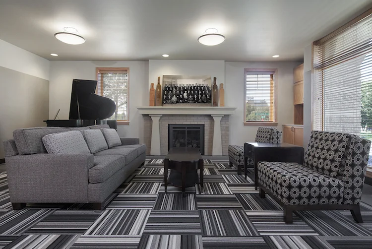 Living room with gray sofas, a grand piano, fireplace and striped carpet tile