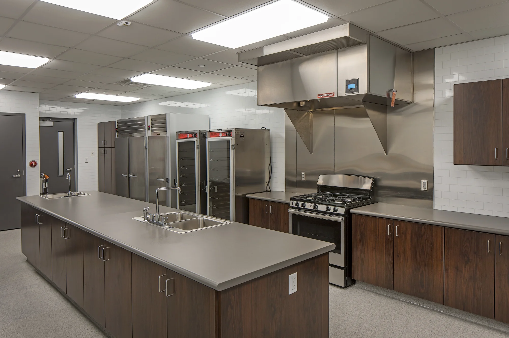 Commercial kitchen with stainless appliances, dark cabinets and a gray island