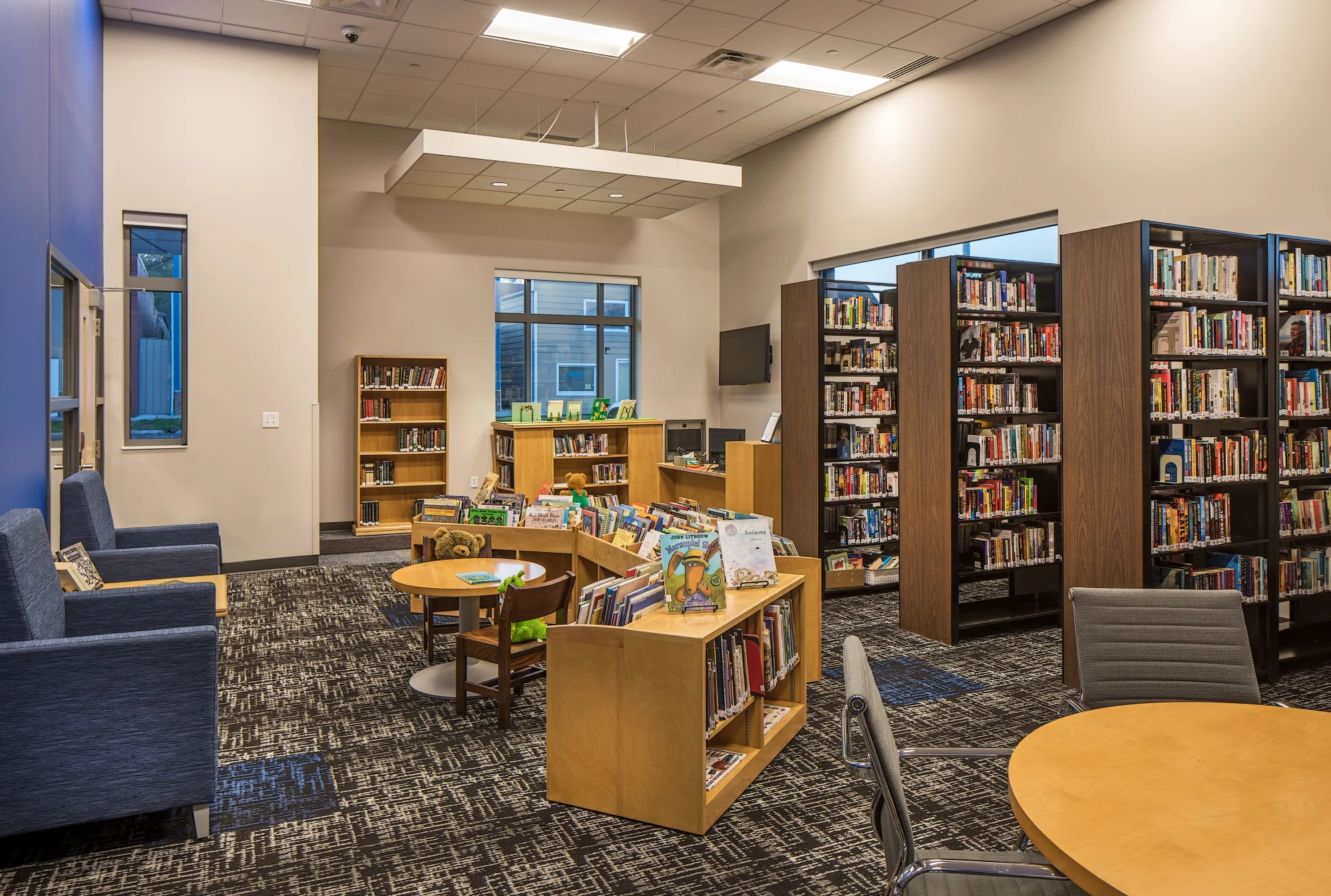 Public library with wood shelving, blue lounge chairs and a children's area