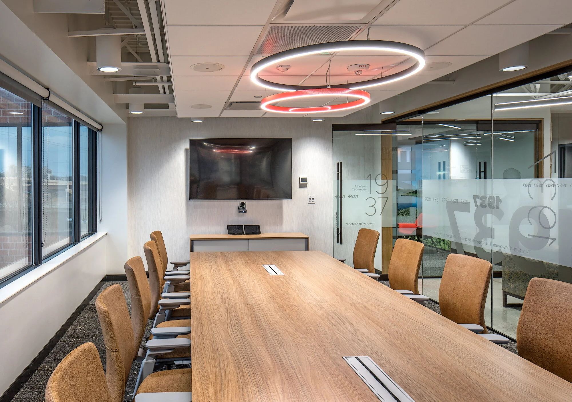 Conference room with a wood table, tan chairs and a red ring light fixture