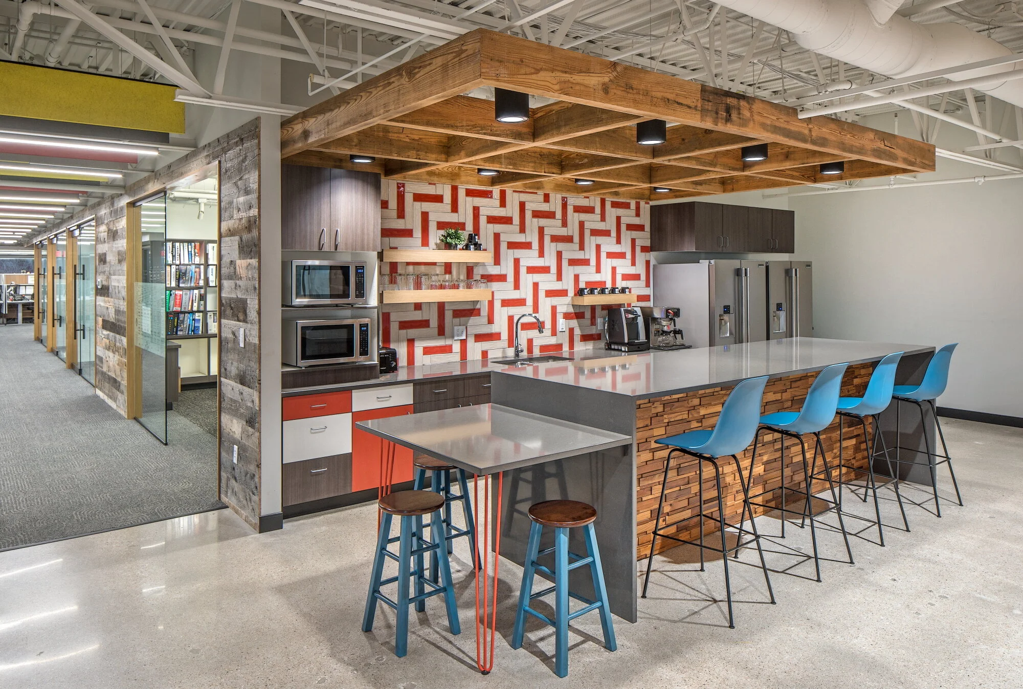 Office cafe with a red and white patterned wall, blue bar stools and a stainless island