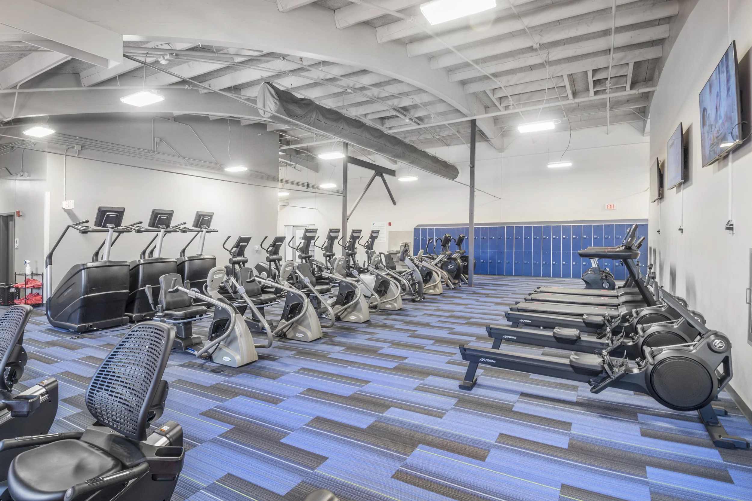 Cardio room with ellipticals, blue striped carpet and lockers