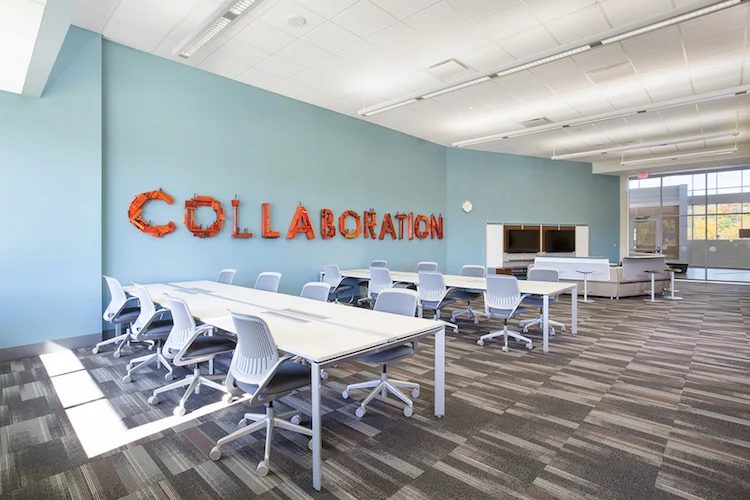 Collaboration room at the UNO Community Engagement Center with a large mural word, white tables and rolling chairs