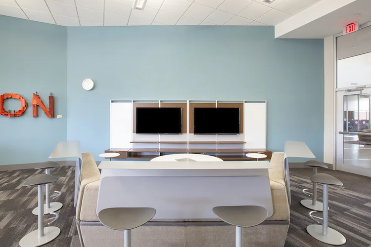Team meeting area with dual monitors, white bar-height table and stools