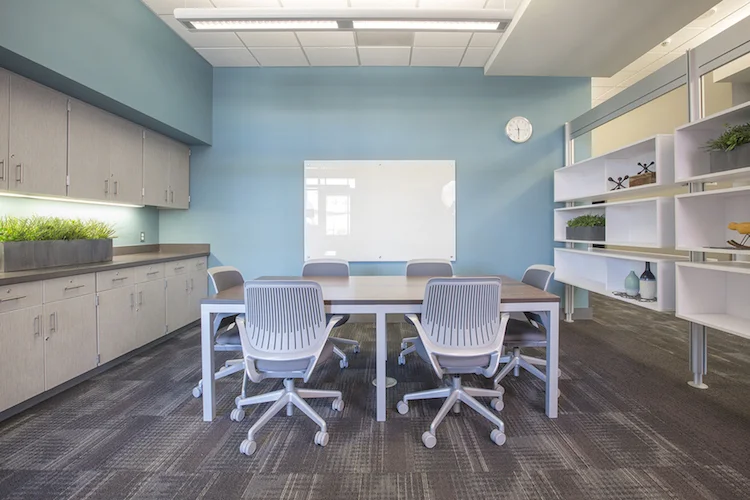 Meeting room with a light blue wall, white table, purple task chairs and open shelving