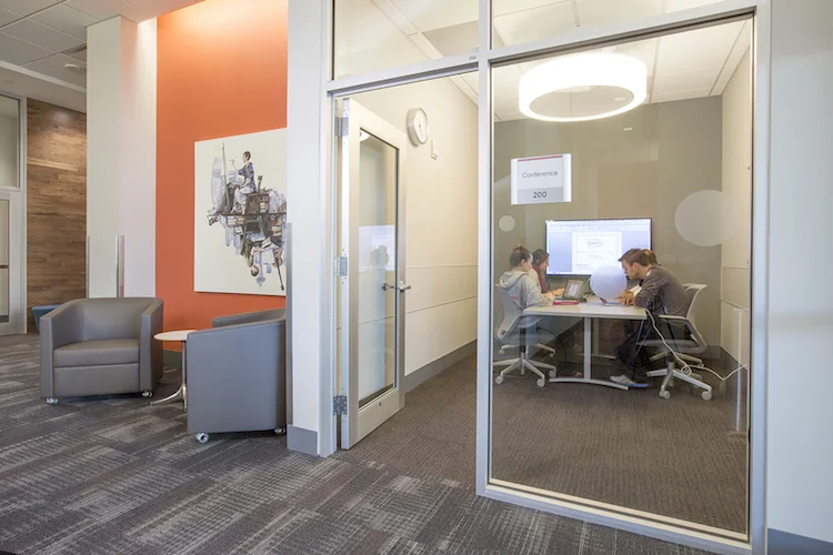 Glass-walled huddle room with an orange accent wall and a lounge chair outside