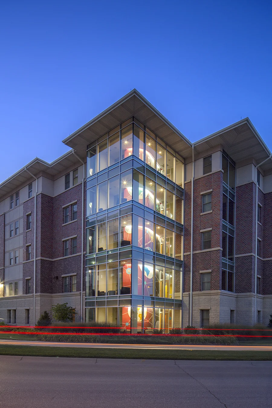 Glass stair tower of Eastside Suites glowing at dusk
