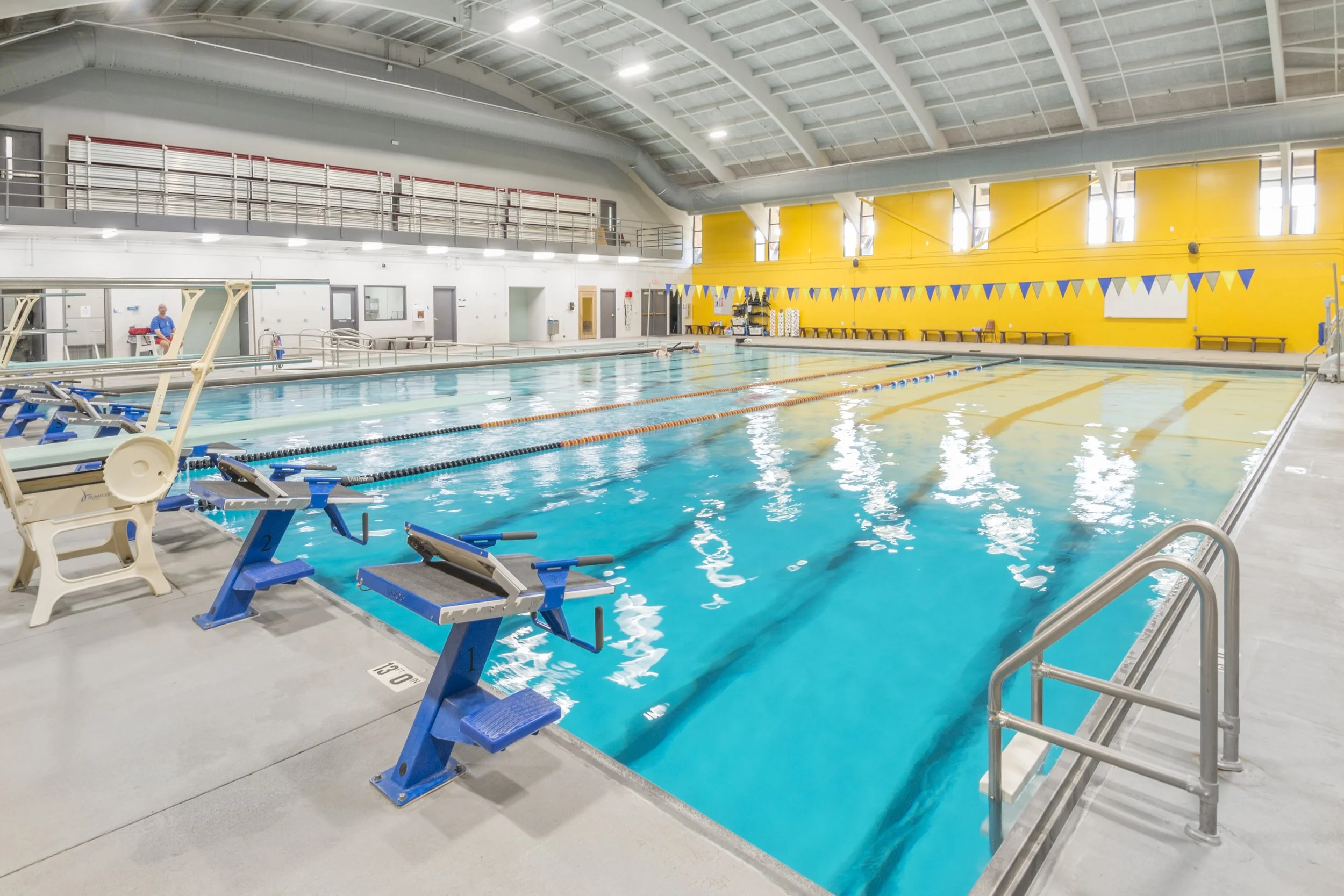 Indoor lap pool at the Hastings YMCA with a yellow accent wall and starting blocks